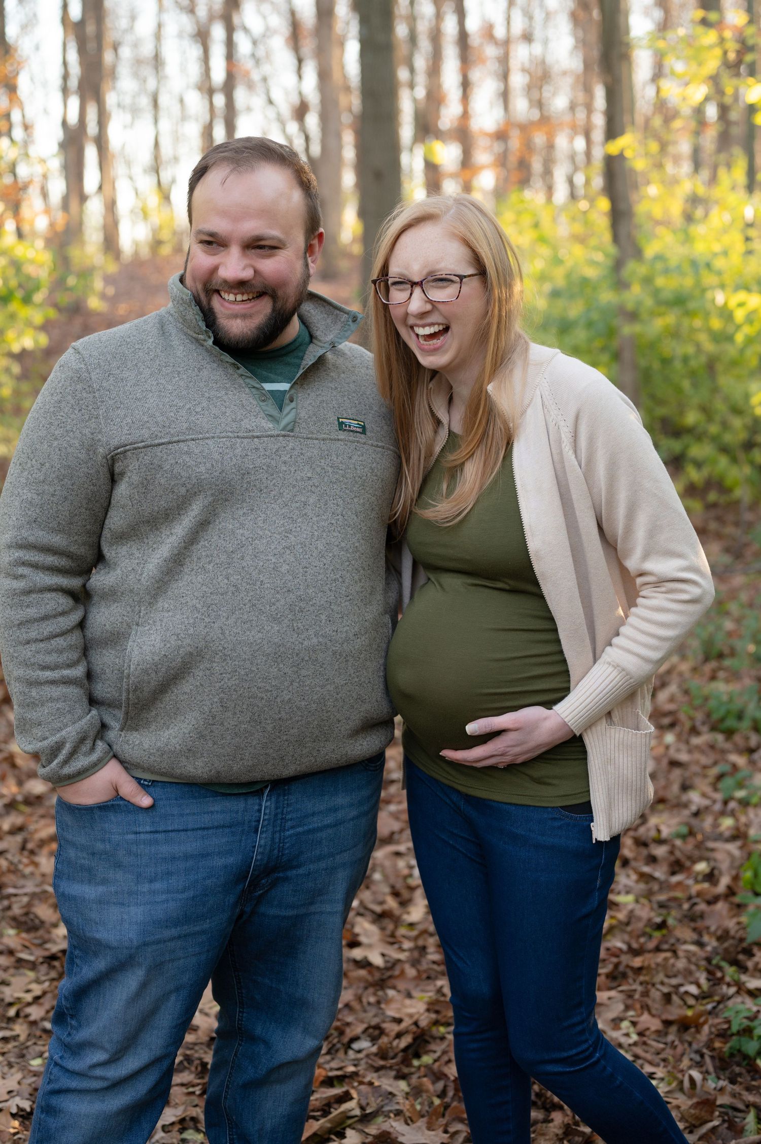 Couple laughing together during outdoor maternity photoshoot in fall forest.