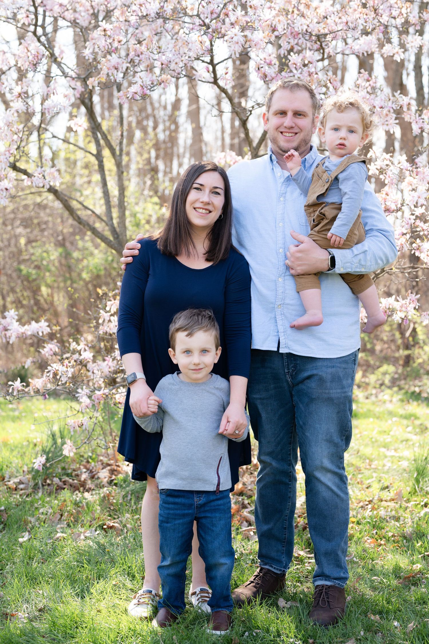 Family of four posed together outdoors with blooming cherry trees and natural lighting.