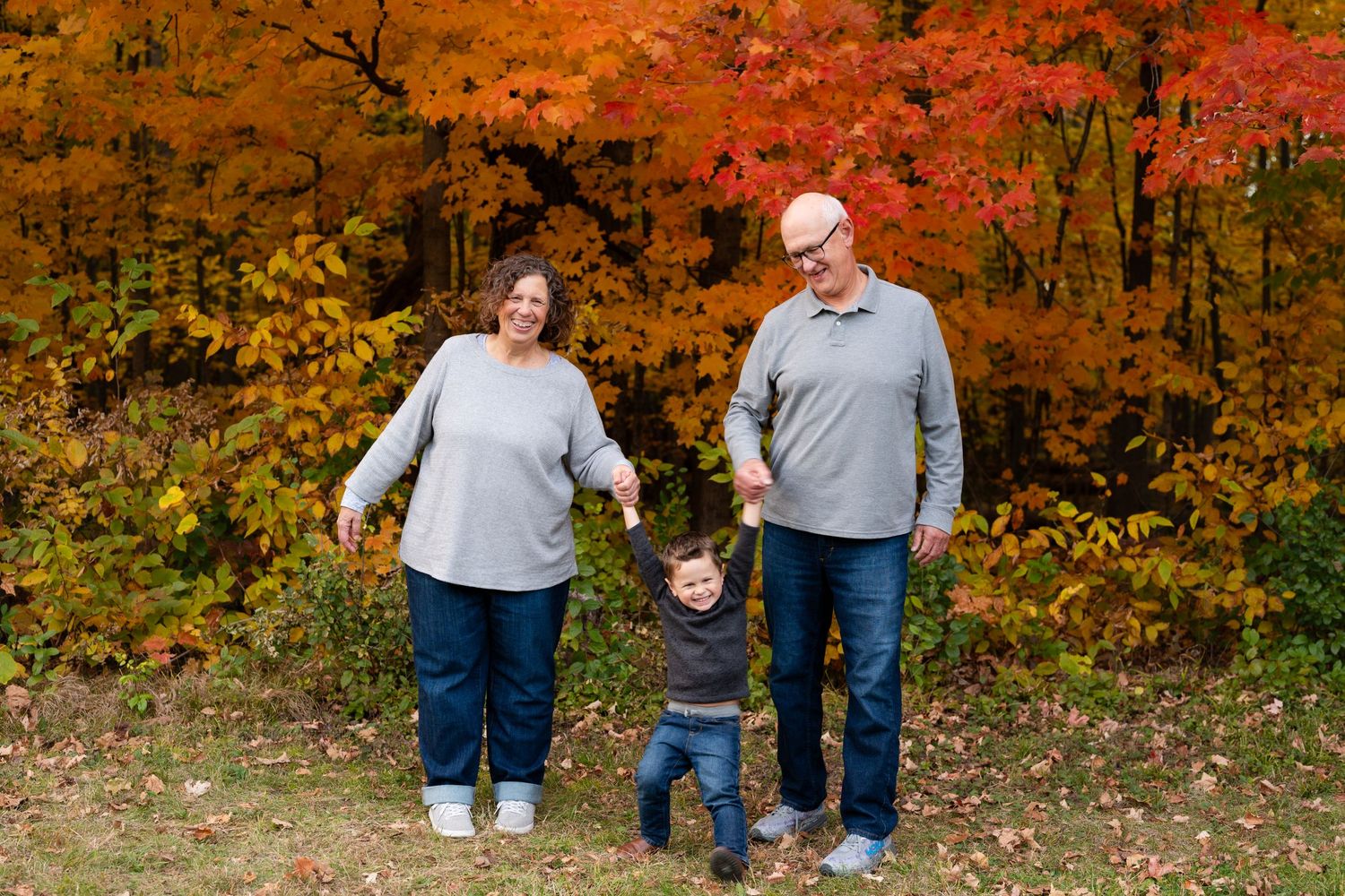 Three people walking hand in hand against a backdrop of bright orange autumn leaves.
