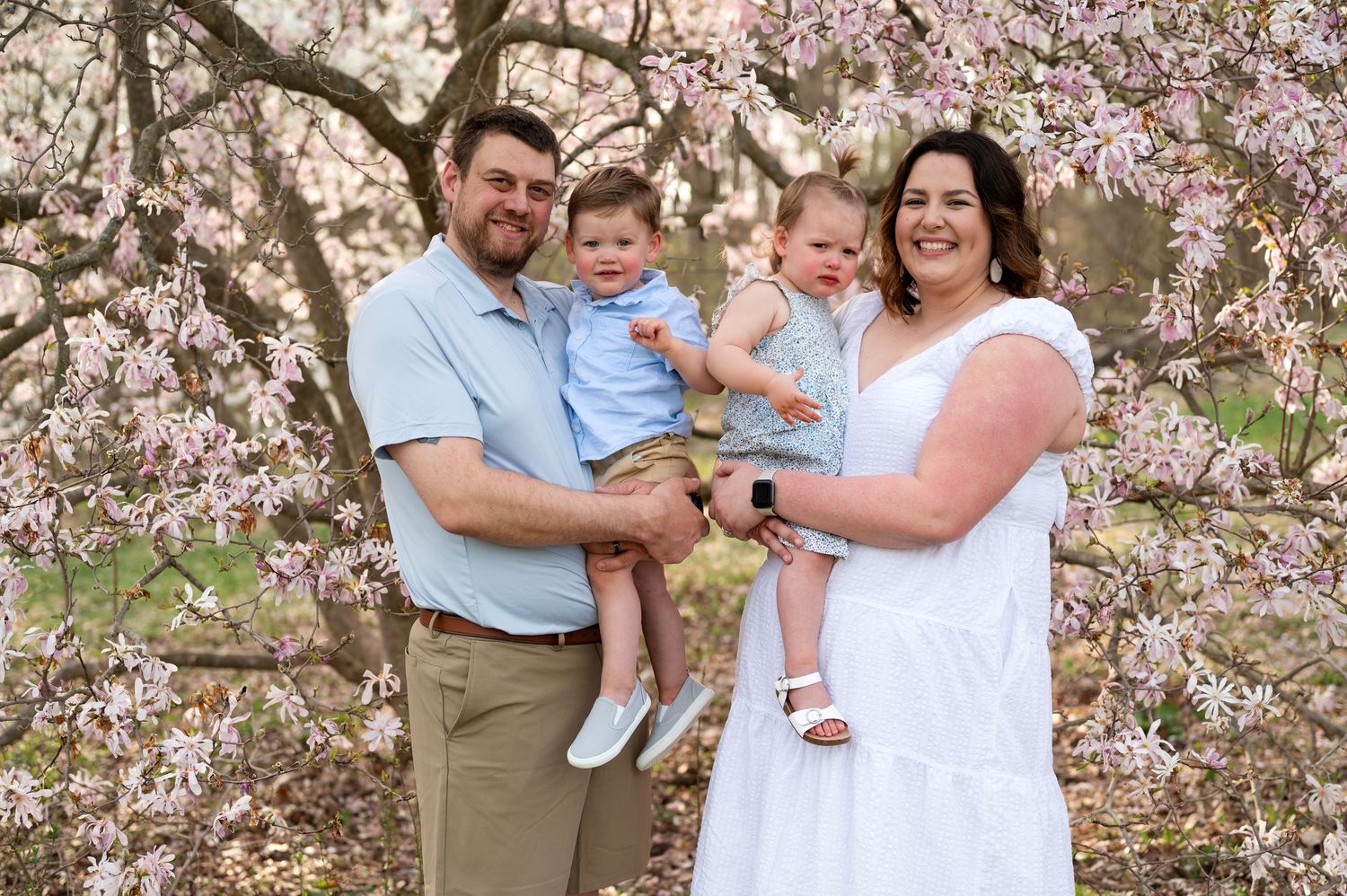 Family poses together under blooming cherry blossom trees during springtime photo session.