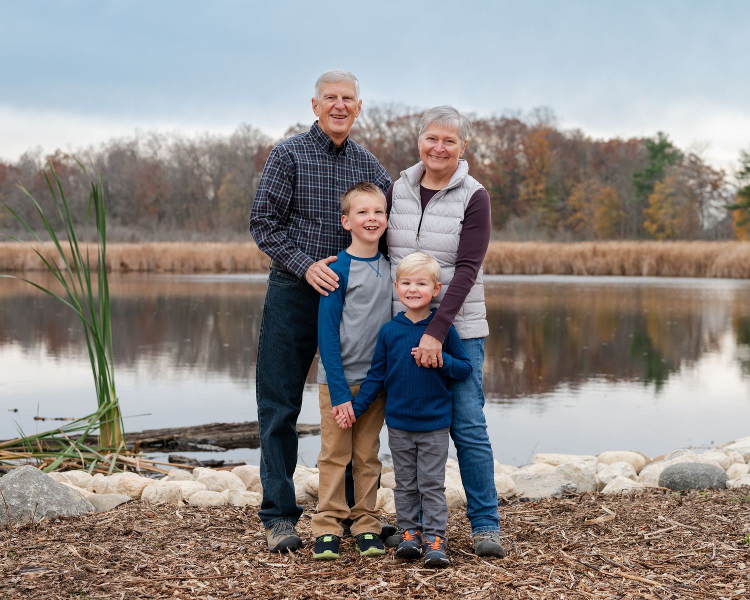 Family group portrait by a serene lake with fall foliage in the background.
