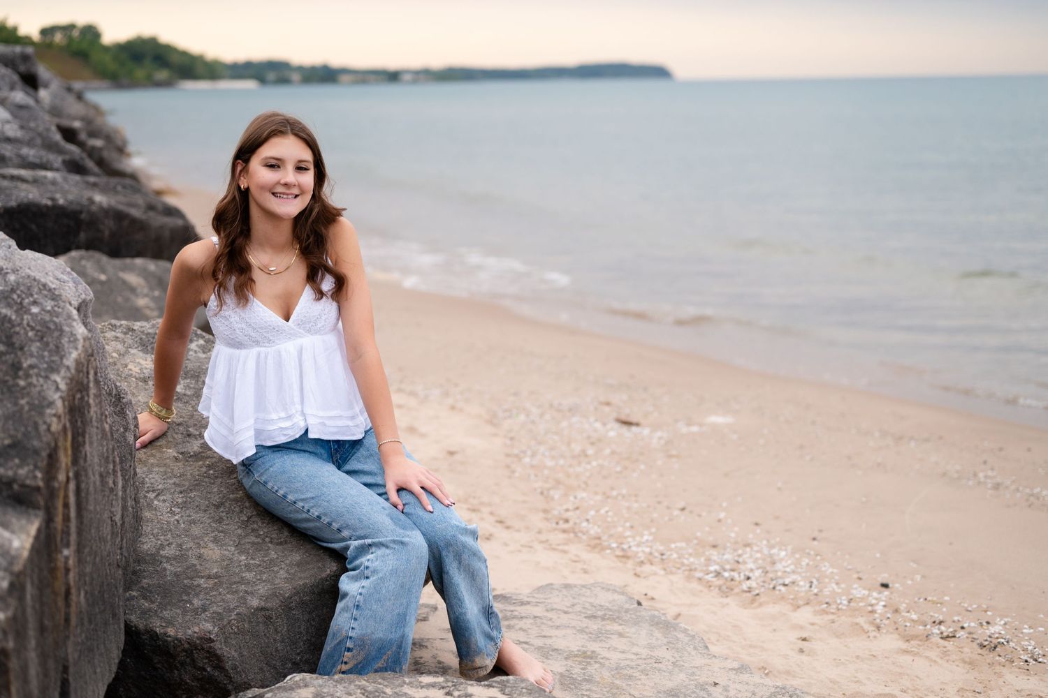 Casual beach portrait sitting on rocky shoreline with water in background.