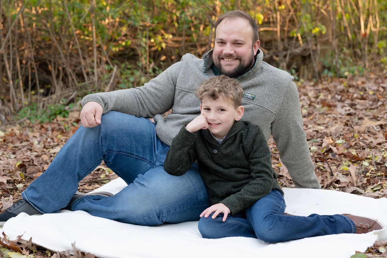 A heartwarming autumn family portrait showing relaxed poses on a white blanket surrounded by fallen leaves.