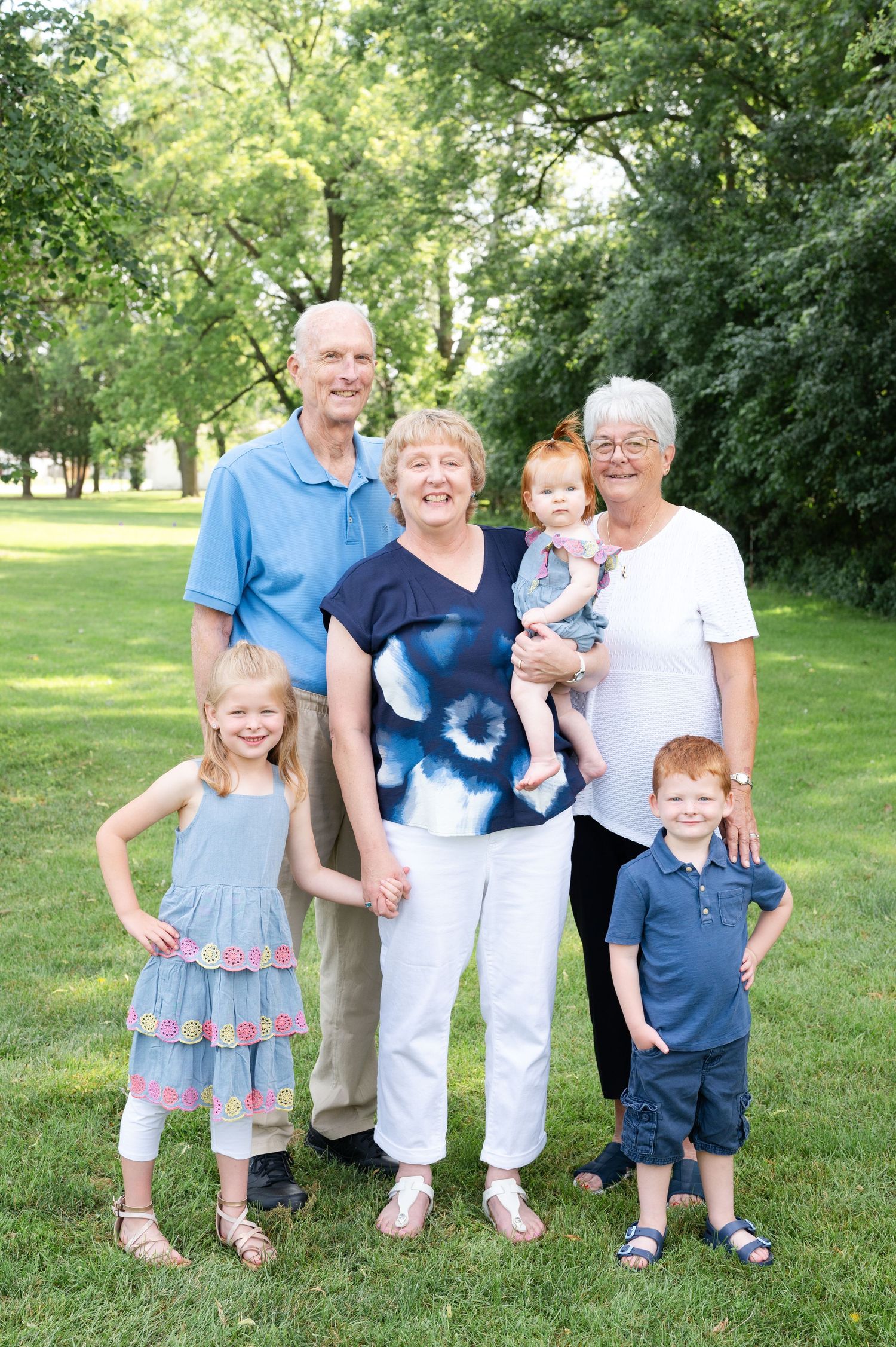 Multi-generational family portrait in a park with children and adults on a sunny summer day.