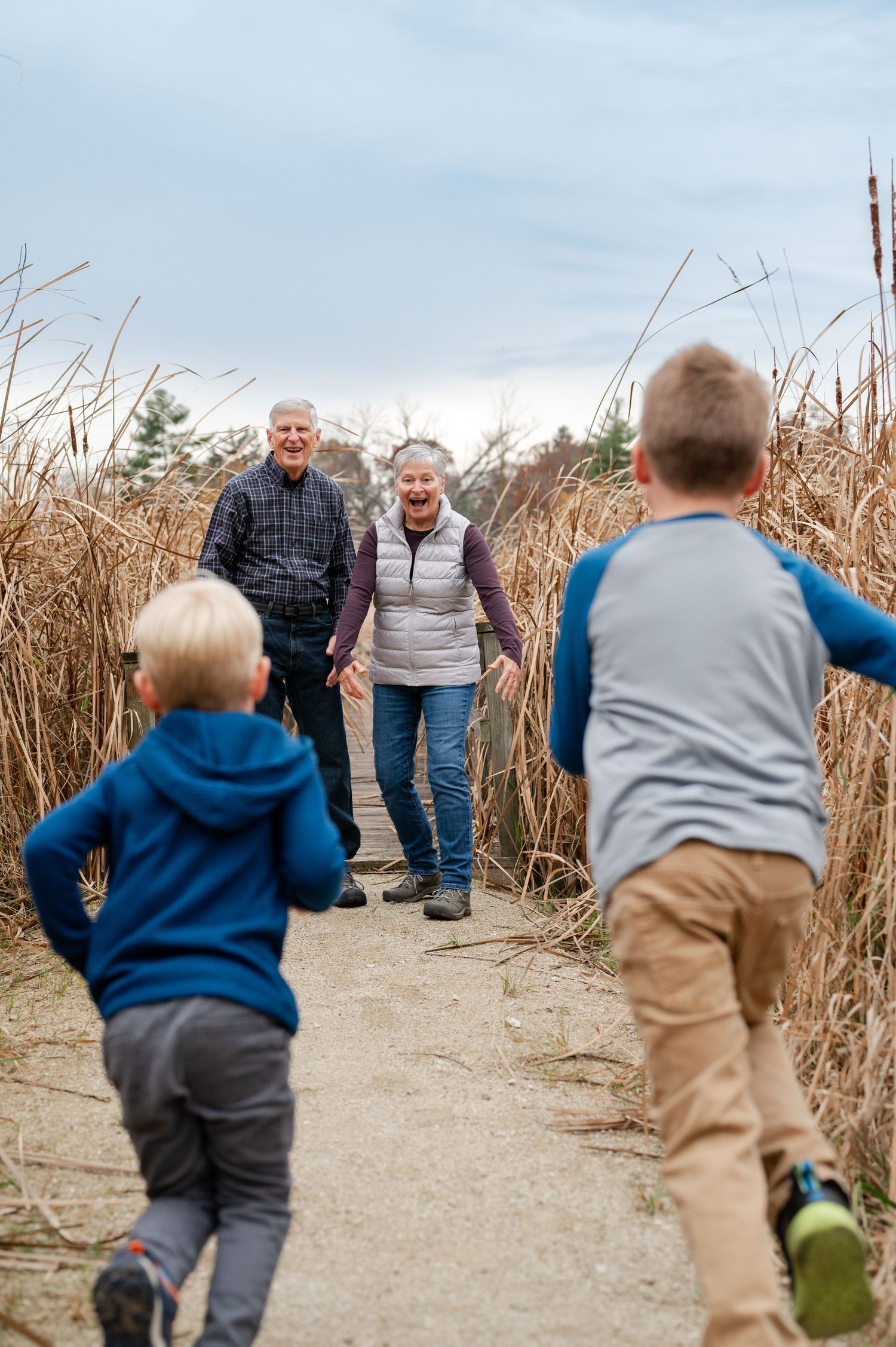 Two children running towards adults on a nature path lined with tall grass.