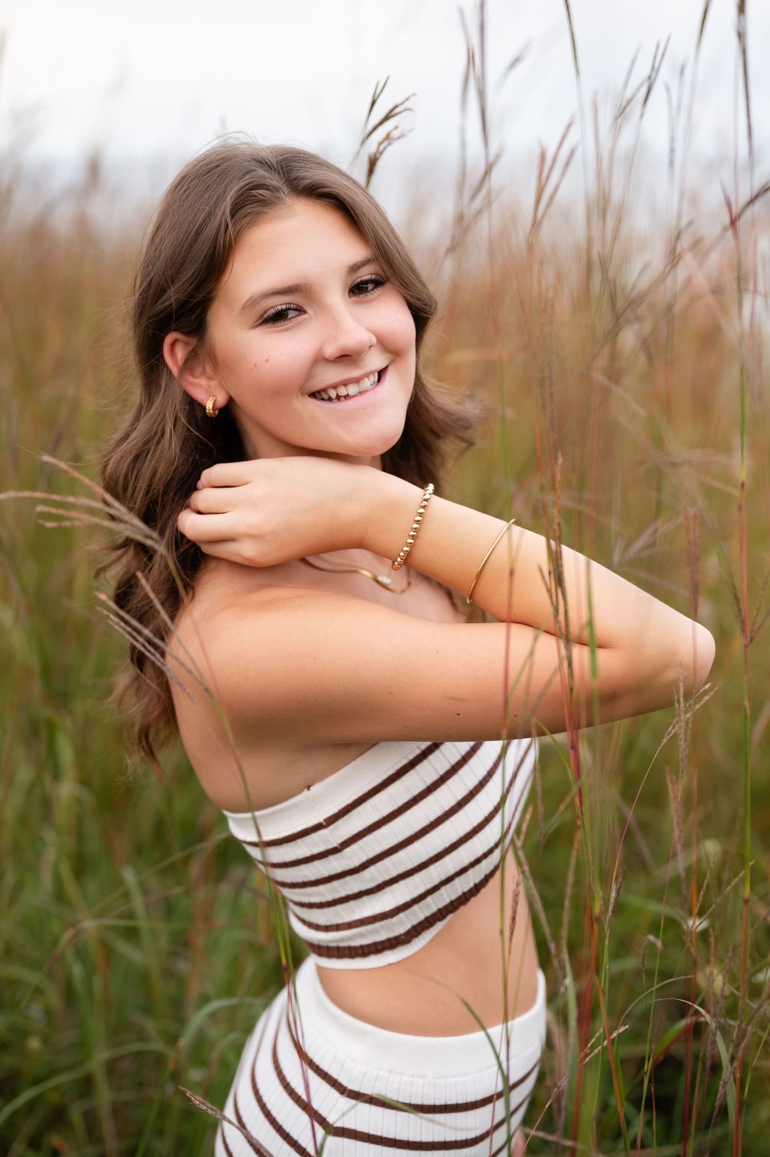 Summer portrait of someone in striped outfit posing in tall grass field.