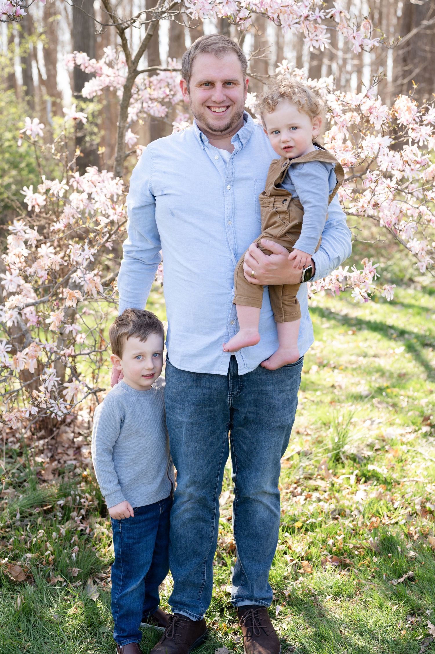 Spring family portrait with light blue shirt and coordinating casual outfits among cherry blossoms.