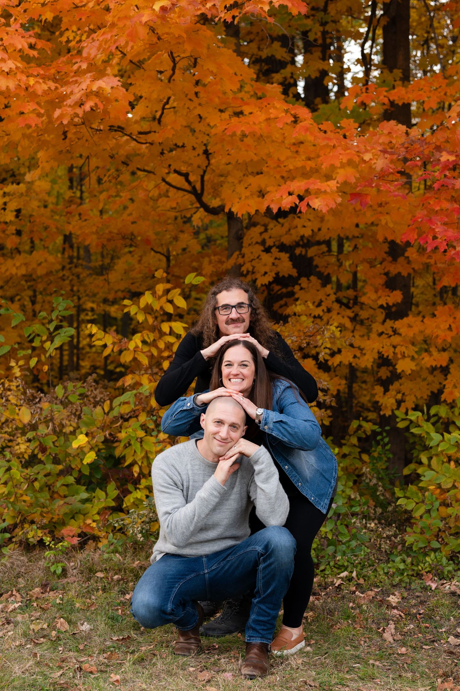 Playful stacked pose of three people against colorful autumn trees.