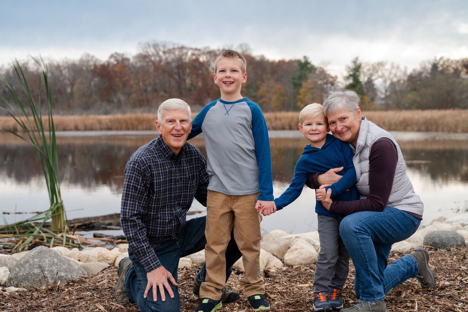 Family of four poses together by a tranquil lake on an autumn day.