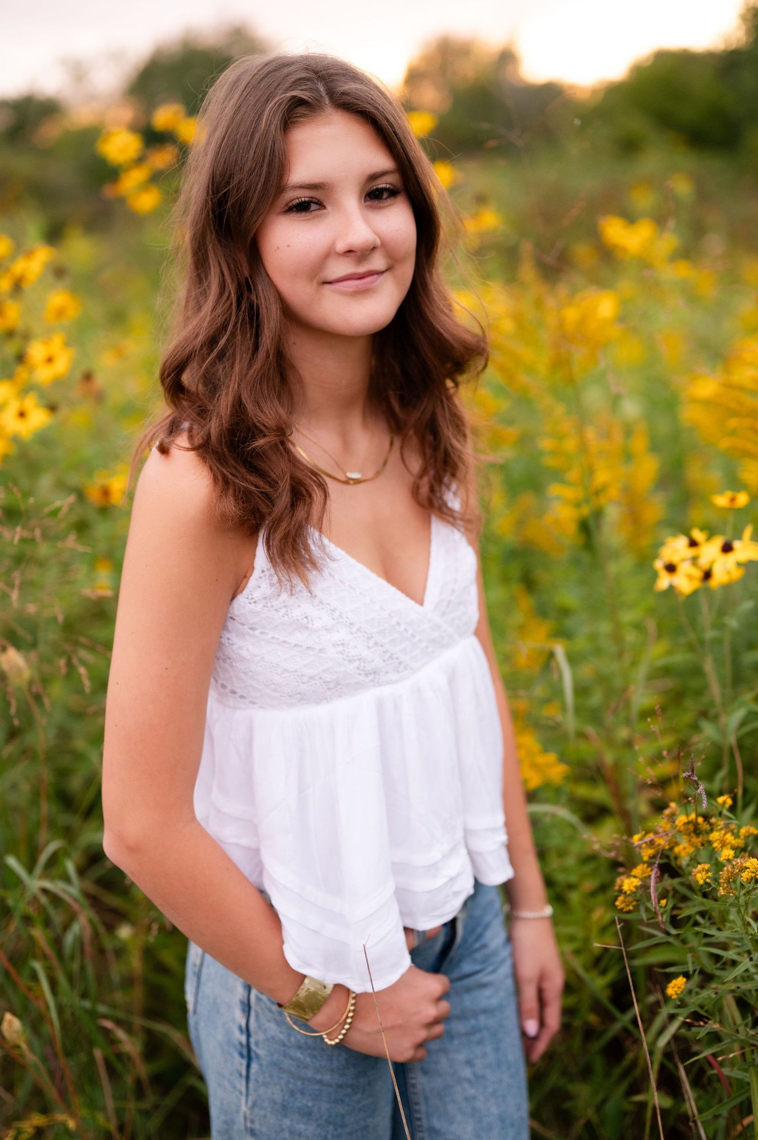Portrait in a field of yellow wildflowers wearing a white lace top.