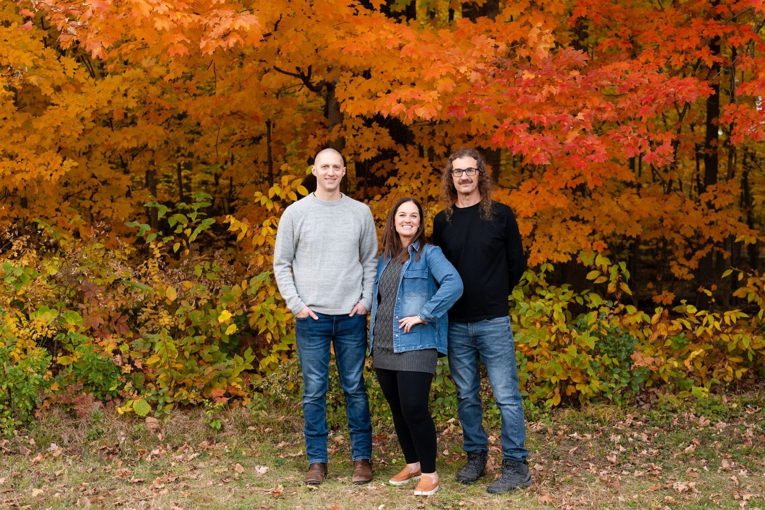 Three people standing together against a backdrop of vivid autumn foliage.