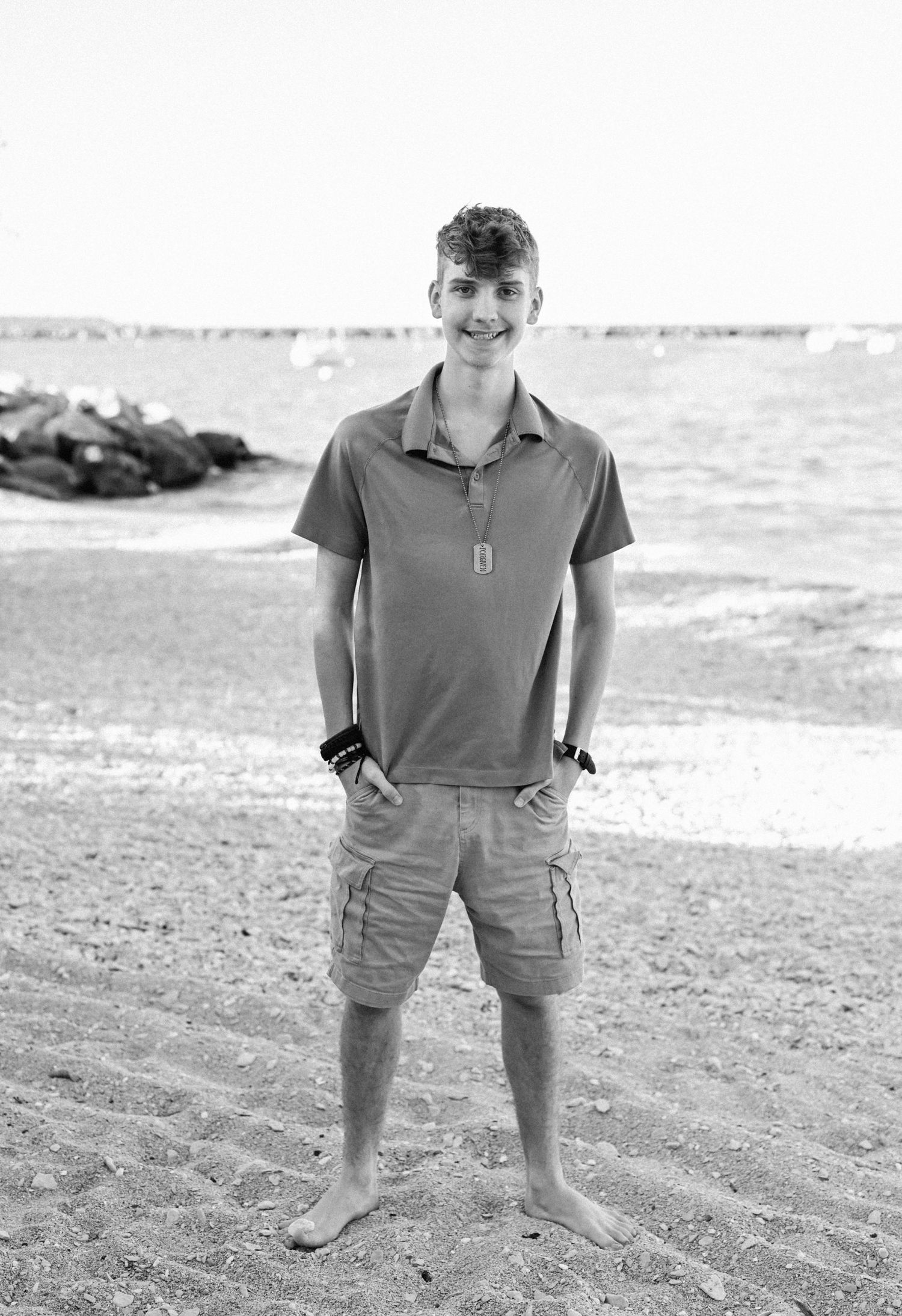 Casual portrait of barefoot person standing on beach wearing polo shirt and cargo shorts.