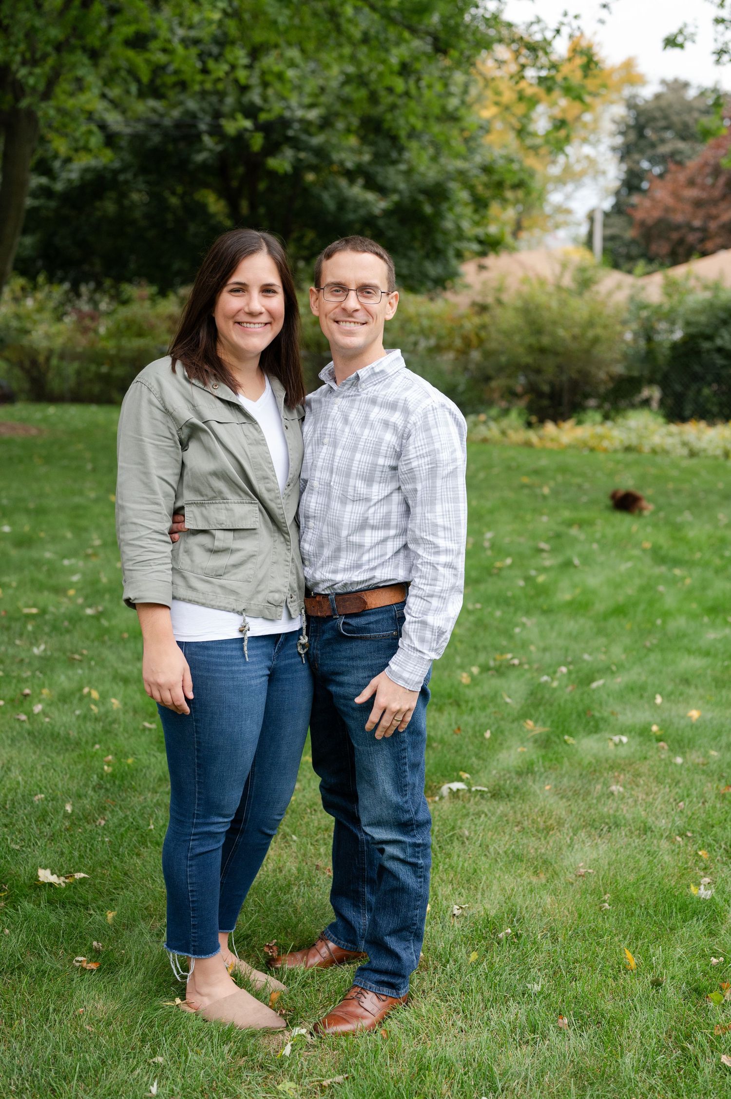 Couple standing together on lawn with fall foliage in background.