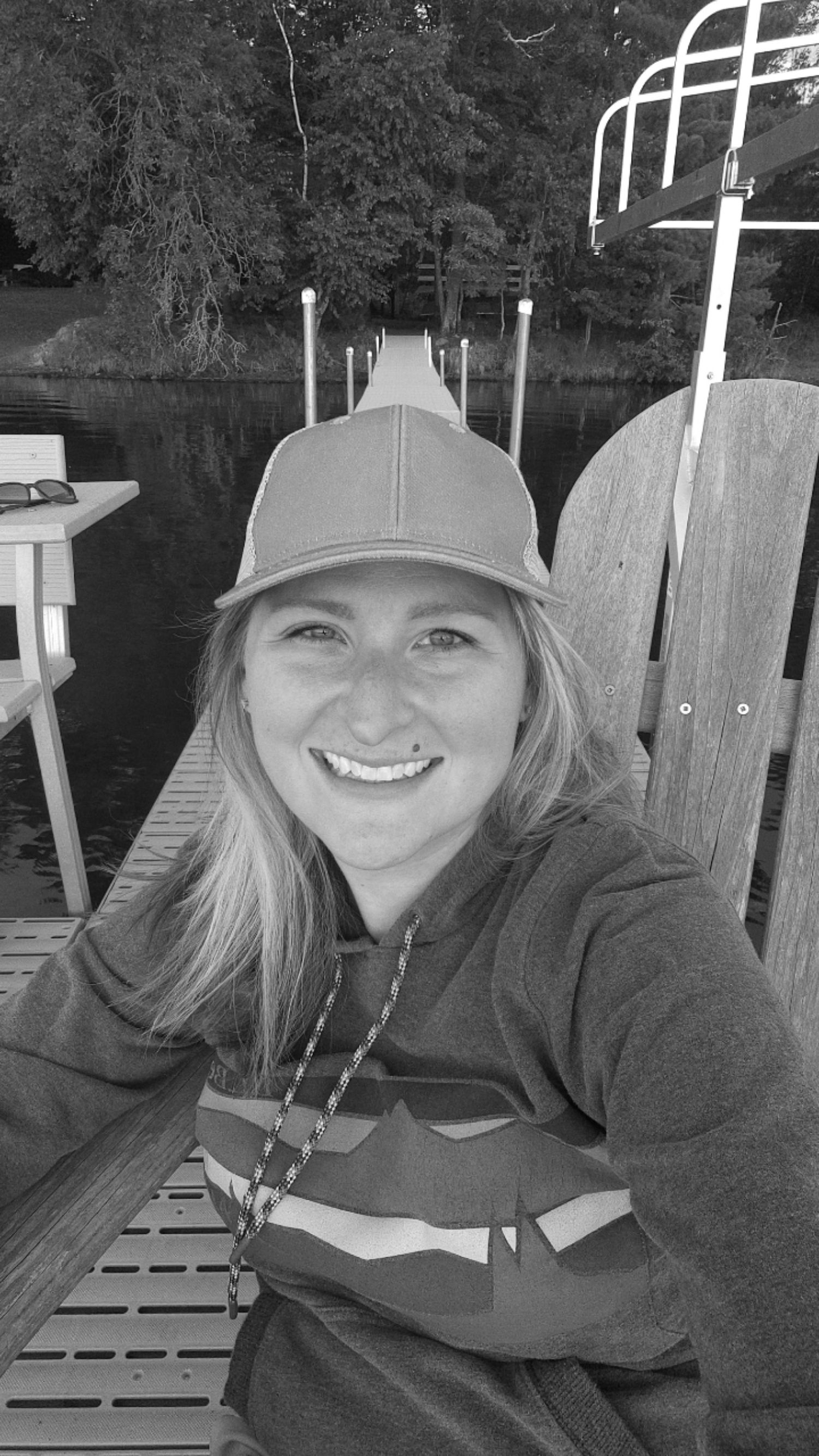 A close-up shot of someone wearing a baseball cap and sweatshirt by a dock.