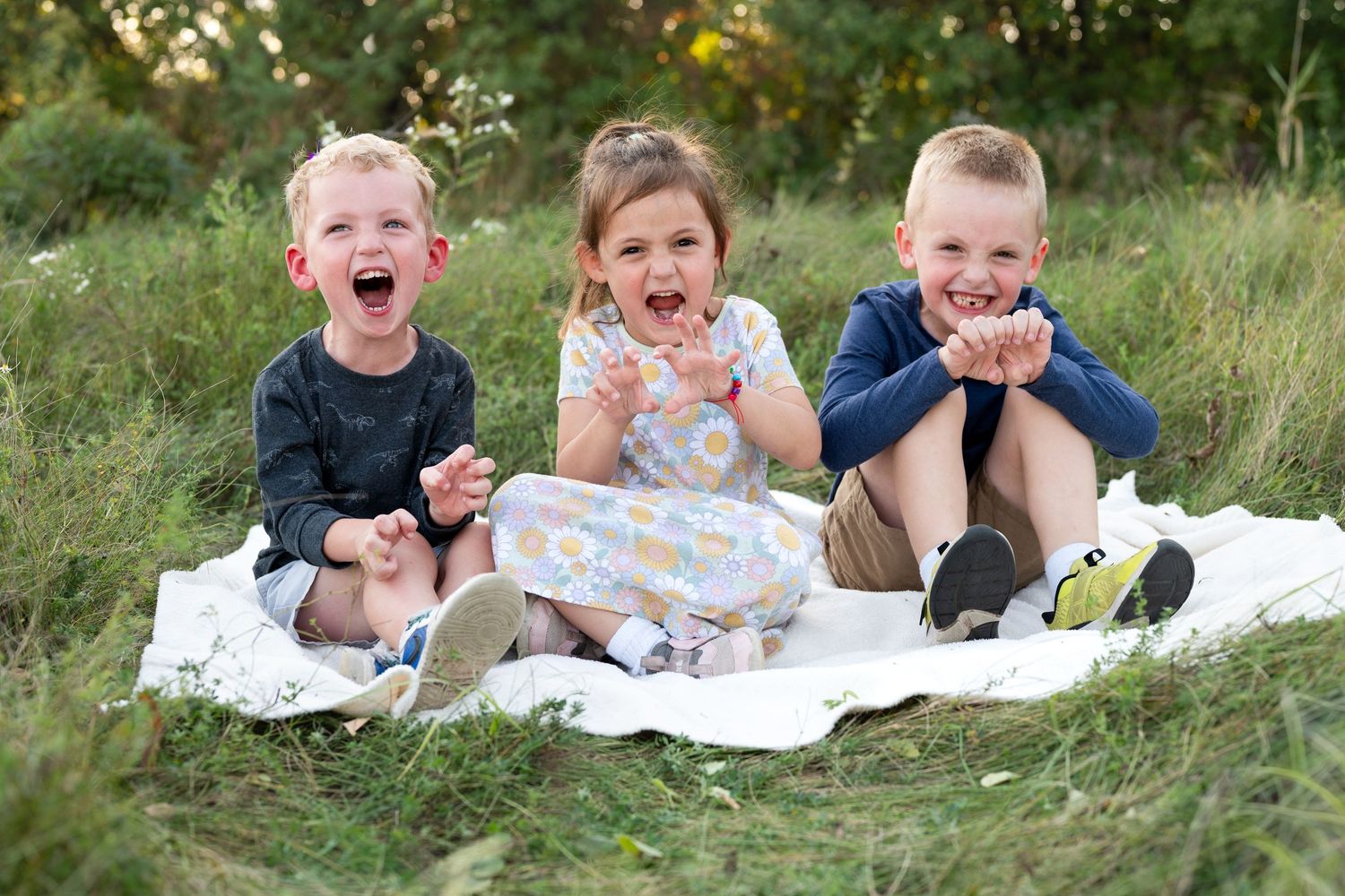 Children lying on grass outdoors laughing and playing together during a sunny day photoshoot.