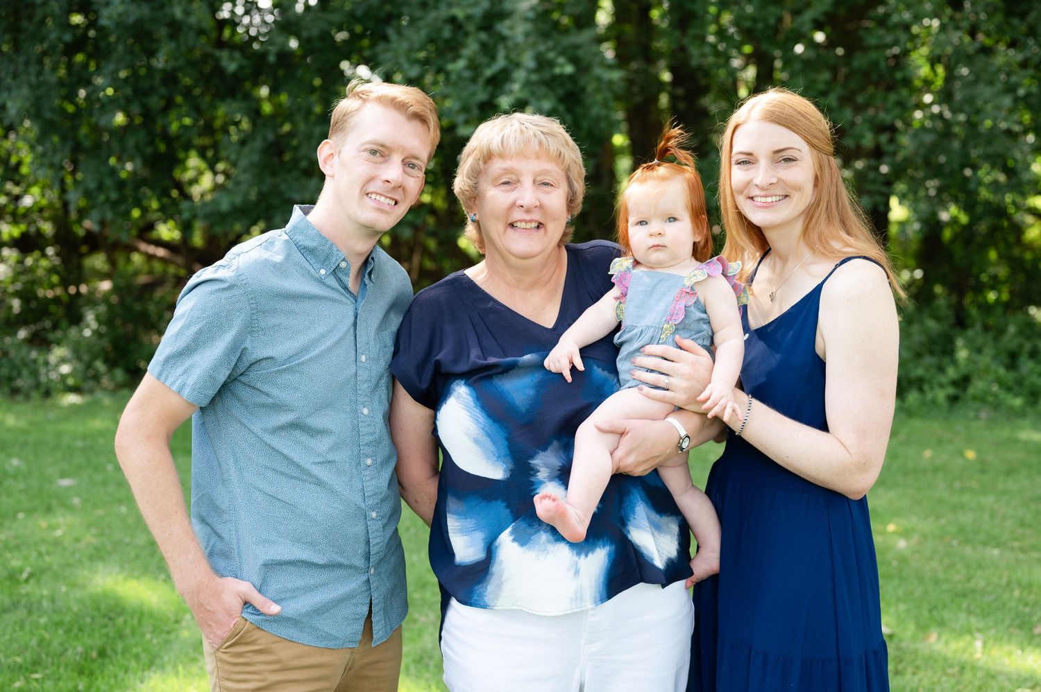 Four people standing together outdoors with trees in background during summer photo session.