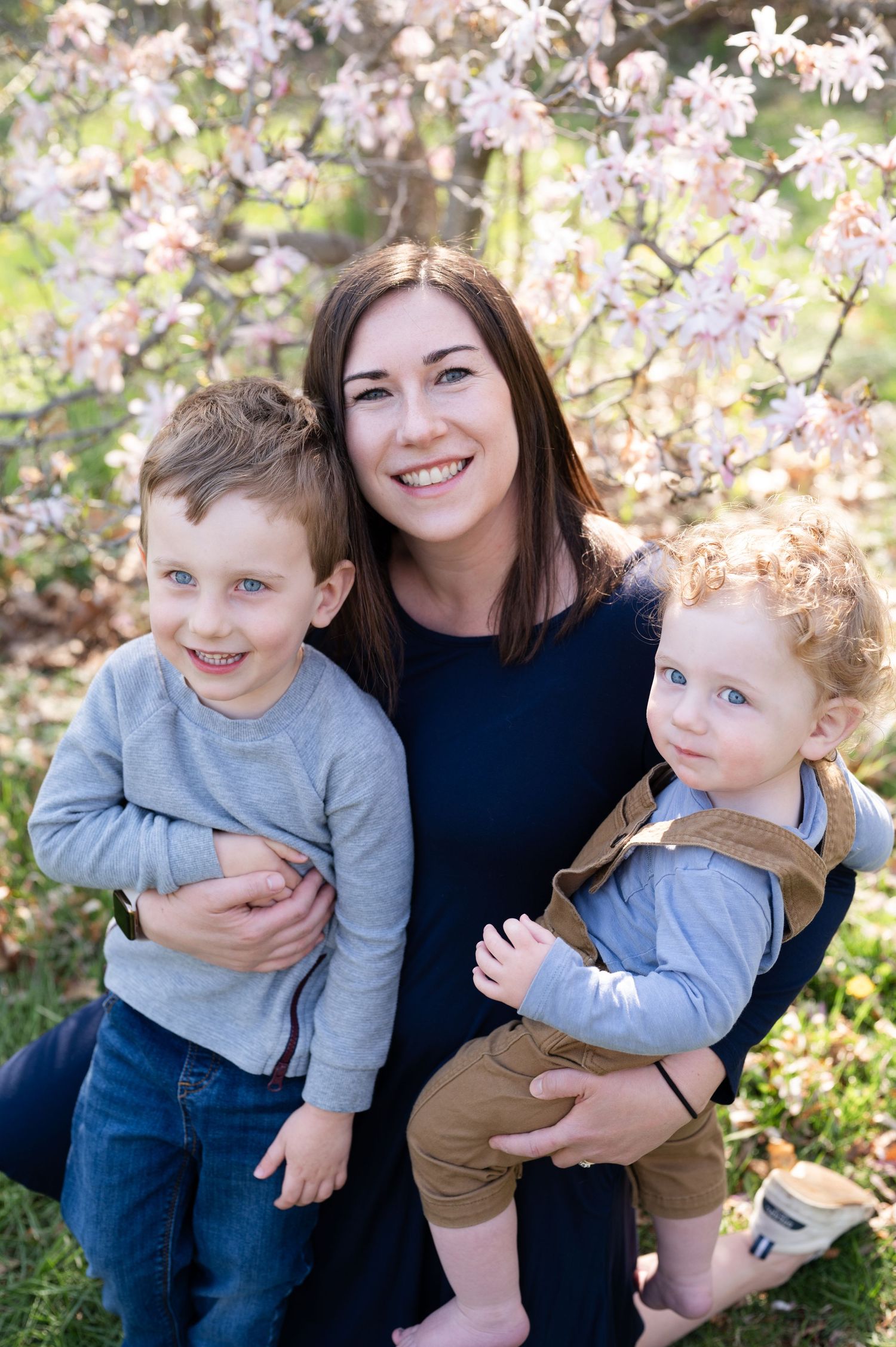 Family portrait with three people posed in front of blooming cherry blossoms.