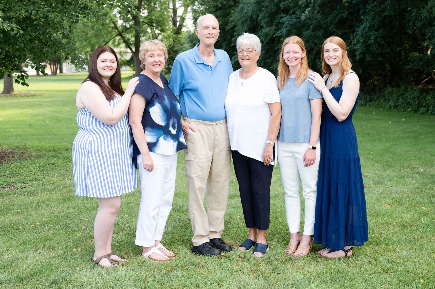 Multi-generational family group poses together outdoors wearing coordinated blue and white clothing.