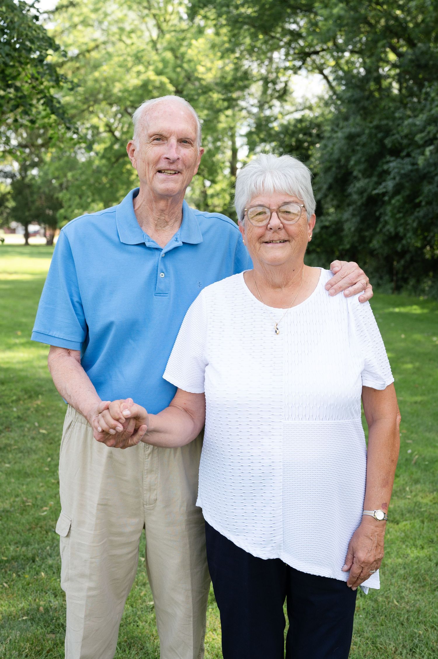 Senior couple in casual attire standing together in a park on a sunny day.