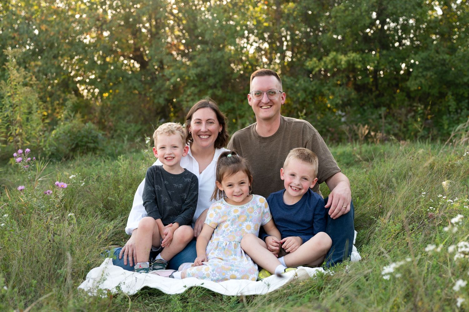 A family relaxes together on a white blanket in a scenic outdoor setting during golden hour.