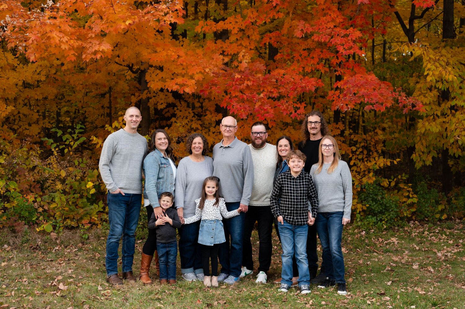 Large family group gathered for portrait with vibrant orange fall foliage in background.