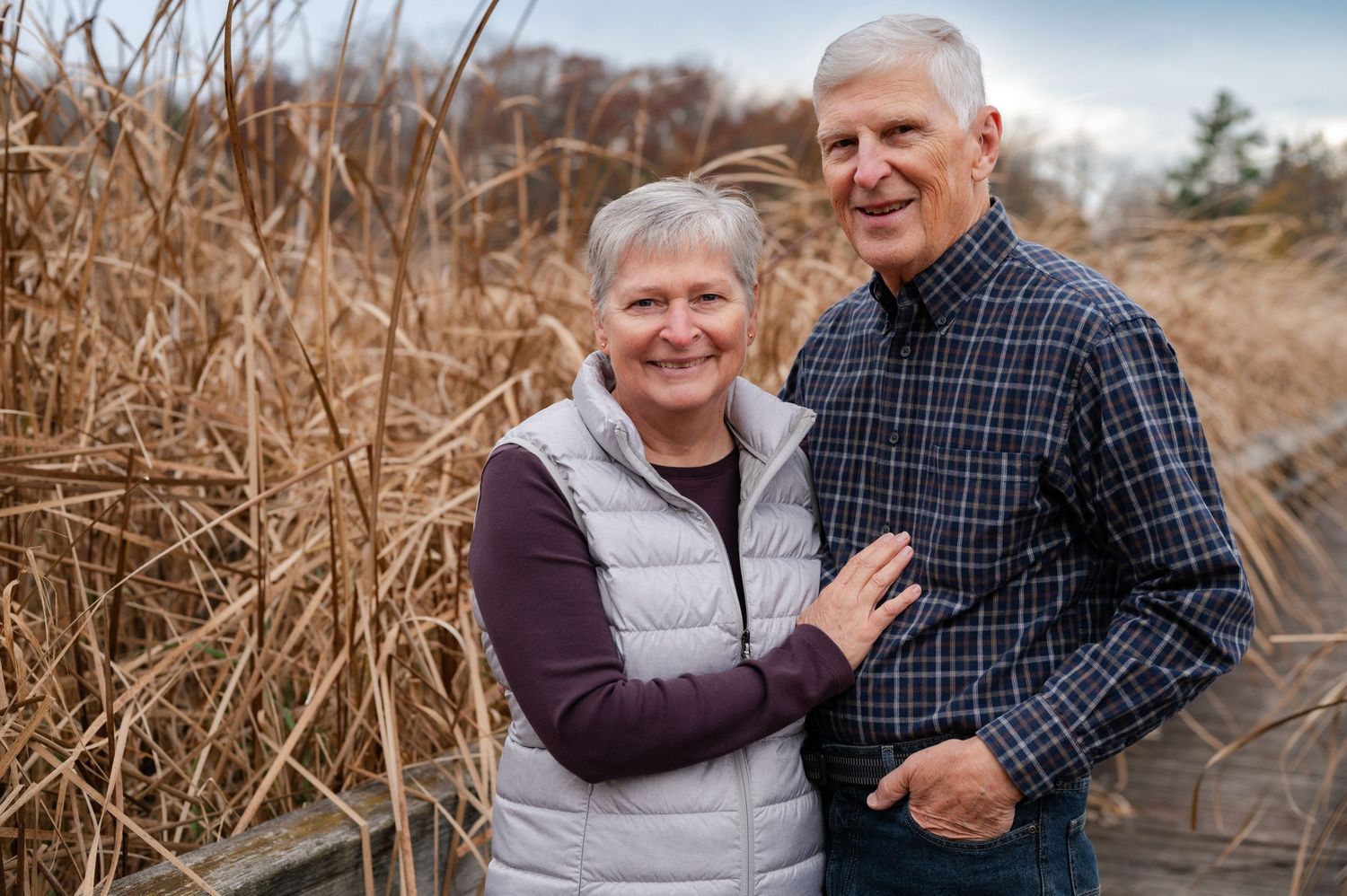 Happy couple posing together on wooden walkway through marsh grasses.
