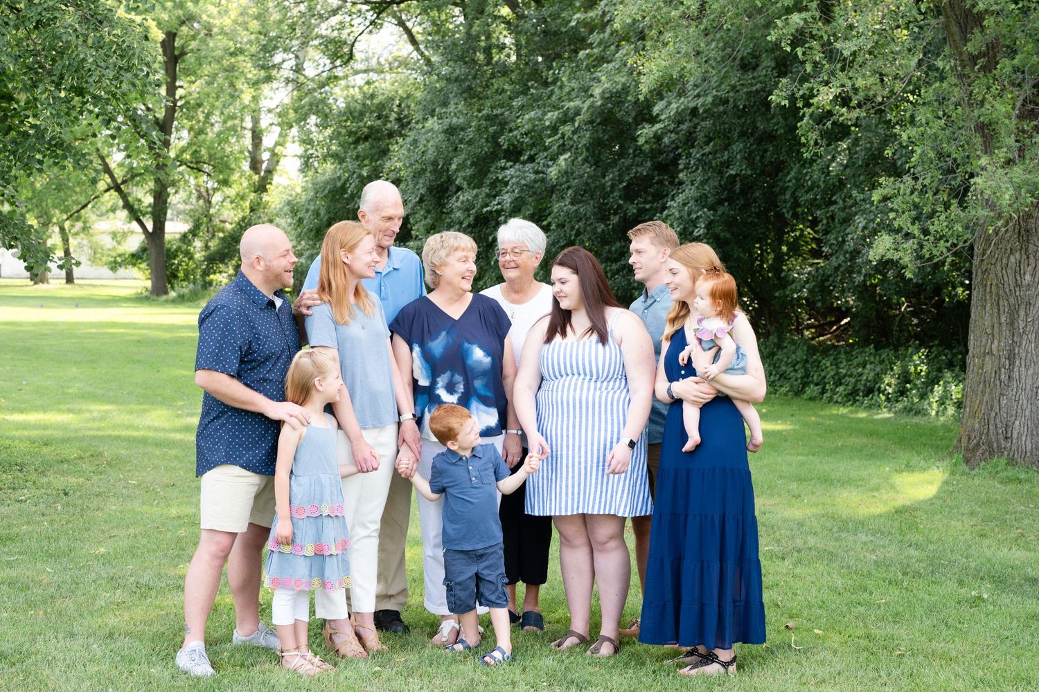 Multi-generational family photo outdoors with adults and children gathered in a park setting.
