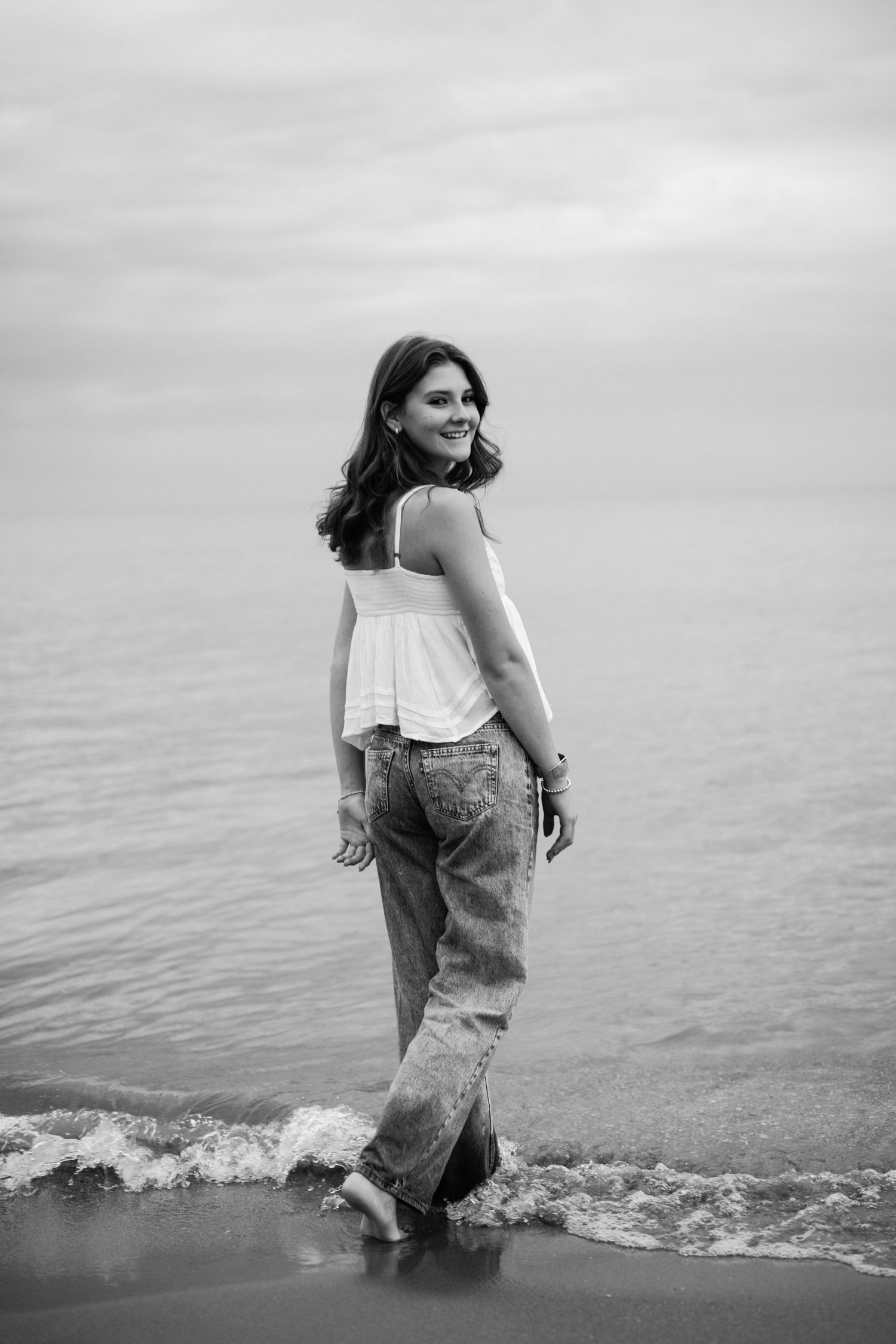 Black and white beach portrait with waves lapping at feet.