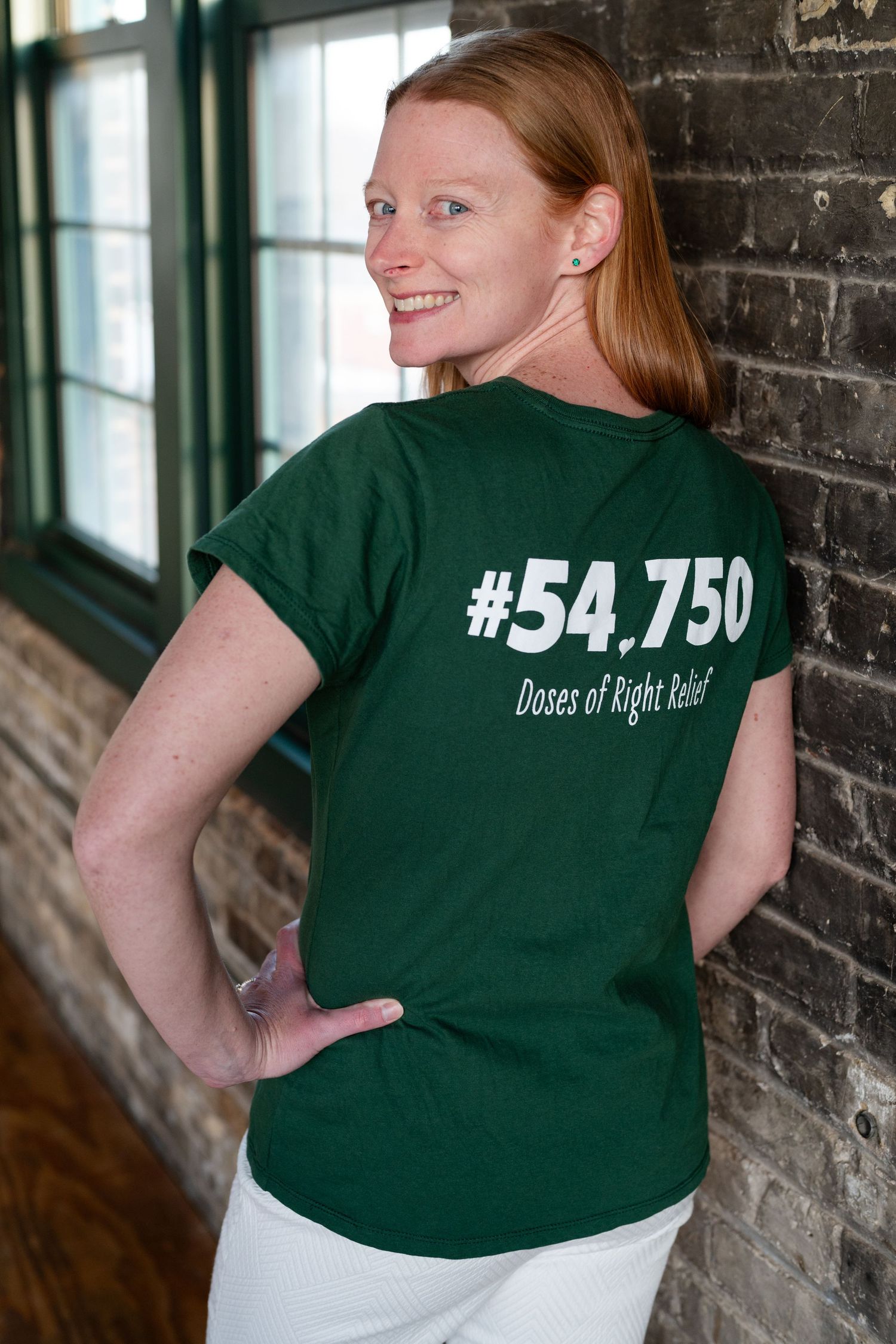 Back view of green t-shirt with #54,750 text against brick wall interior.