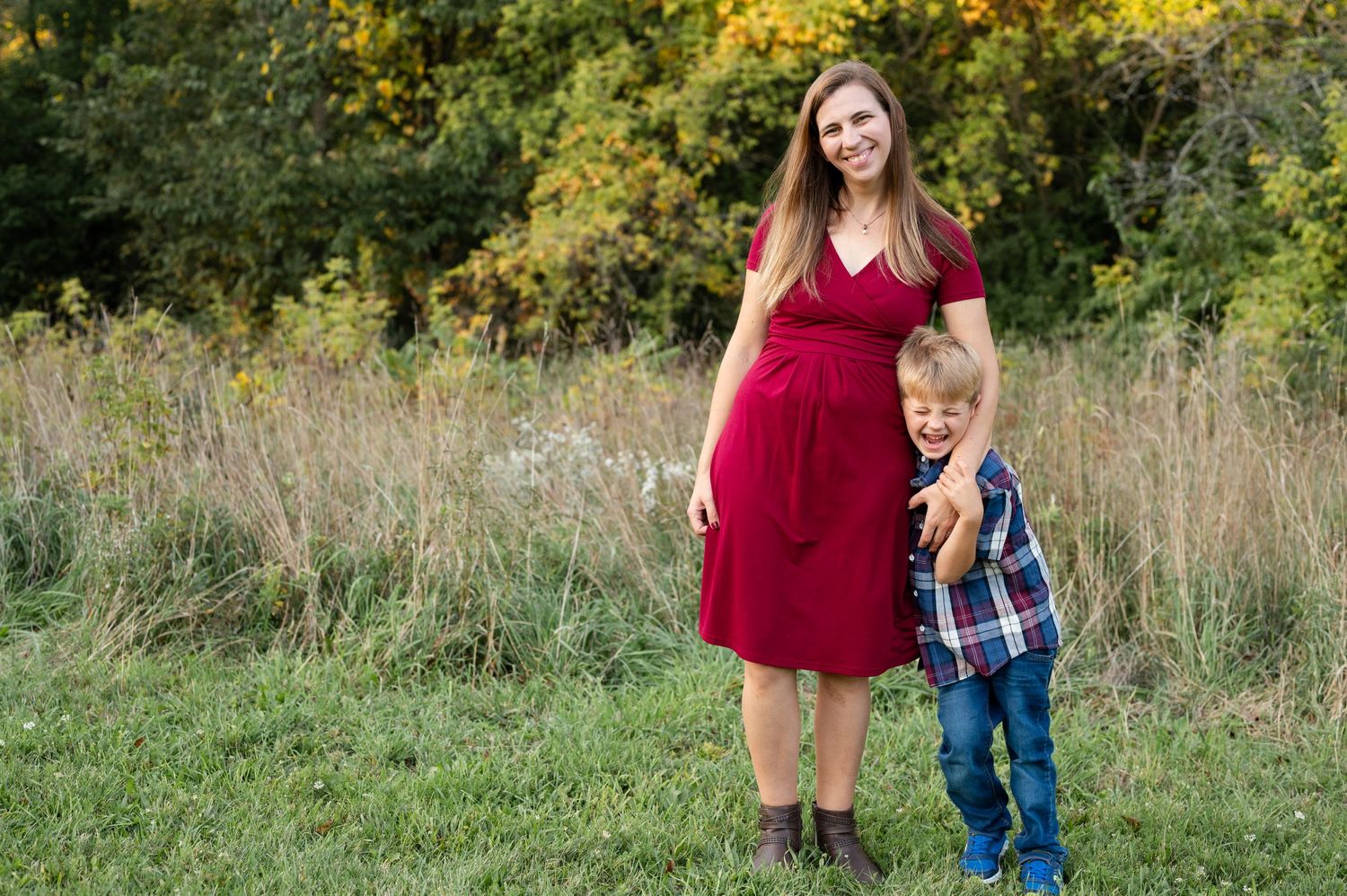 A woman in a red dress and young child stand together in a field of tall grass.