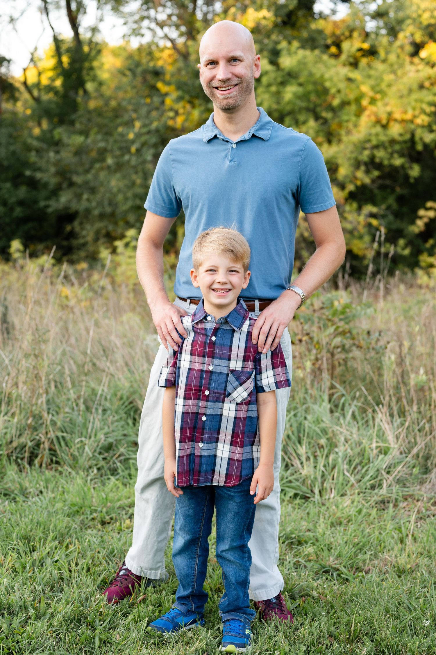 Parent and child standing together outdoors in summer field with tall grass.