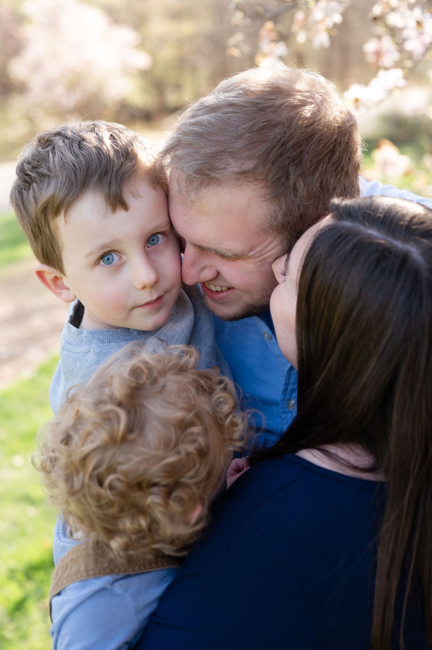 Intimate family embrace captured during spring with cherry blossoms blooming in the background.