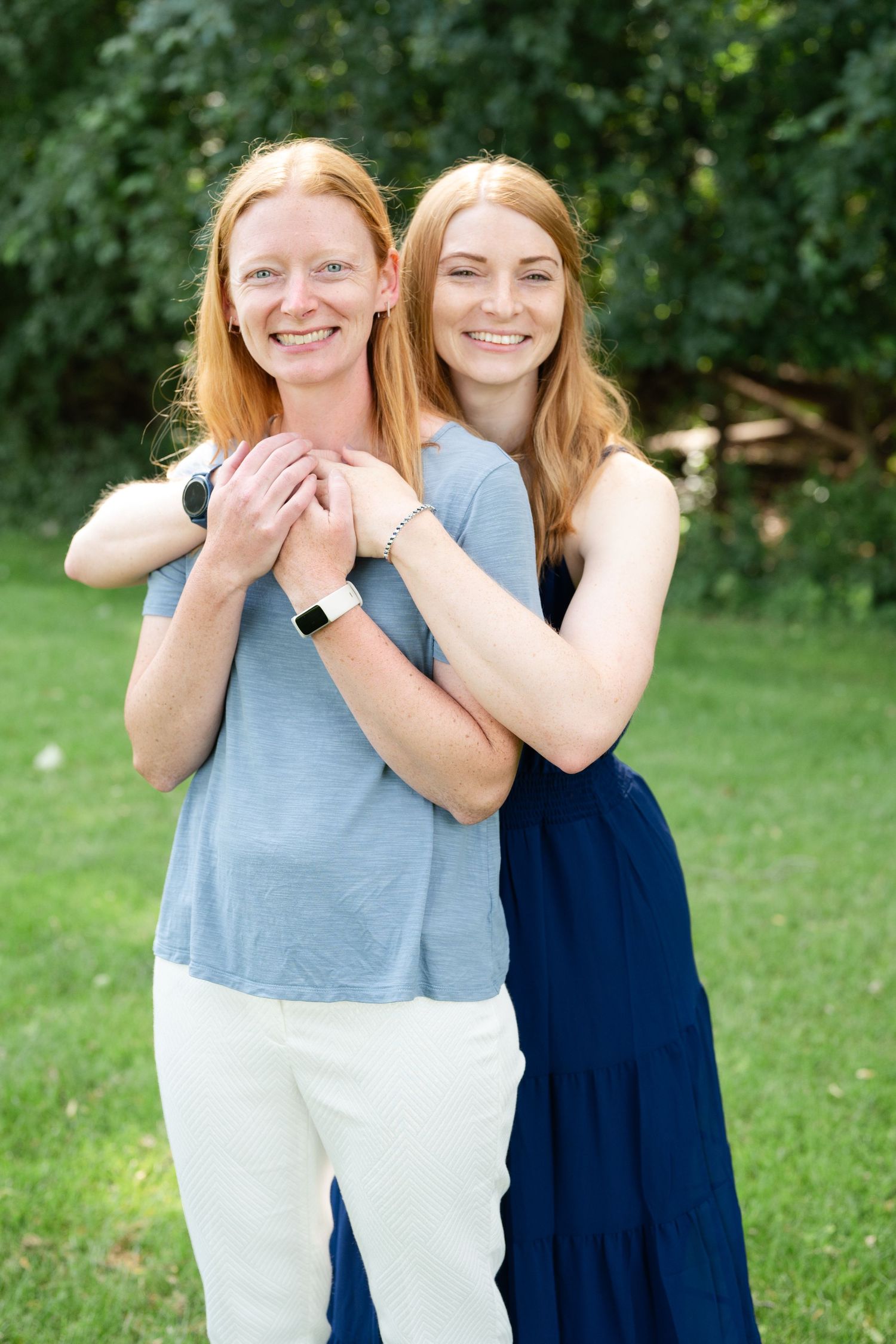 Two people in blue outfits embracing and smiling on a sunny day in a green garden setting.