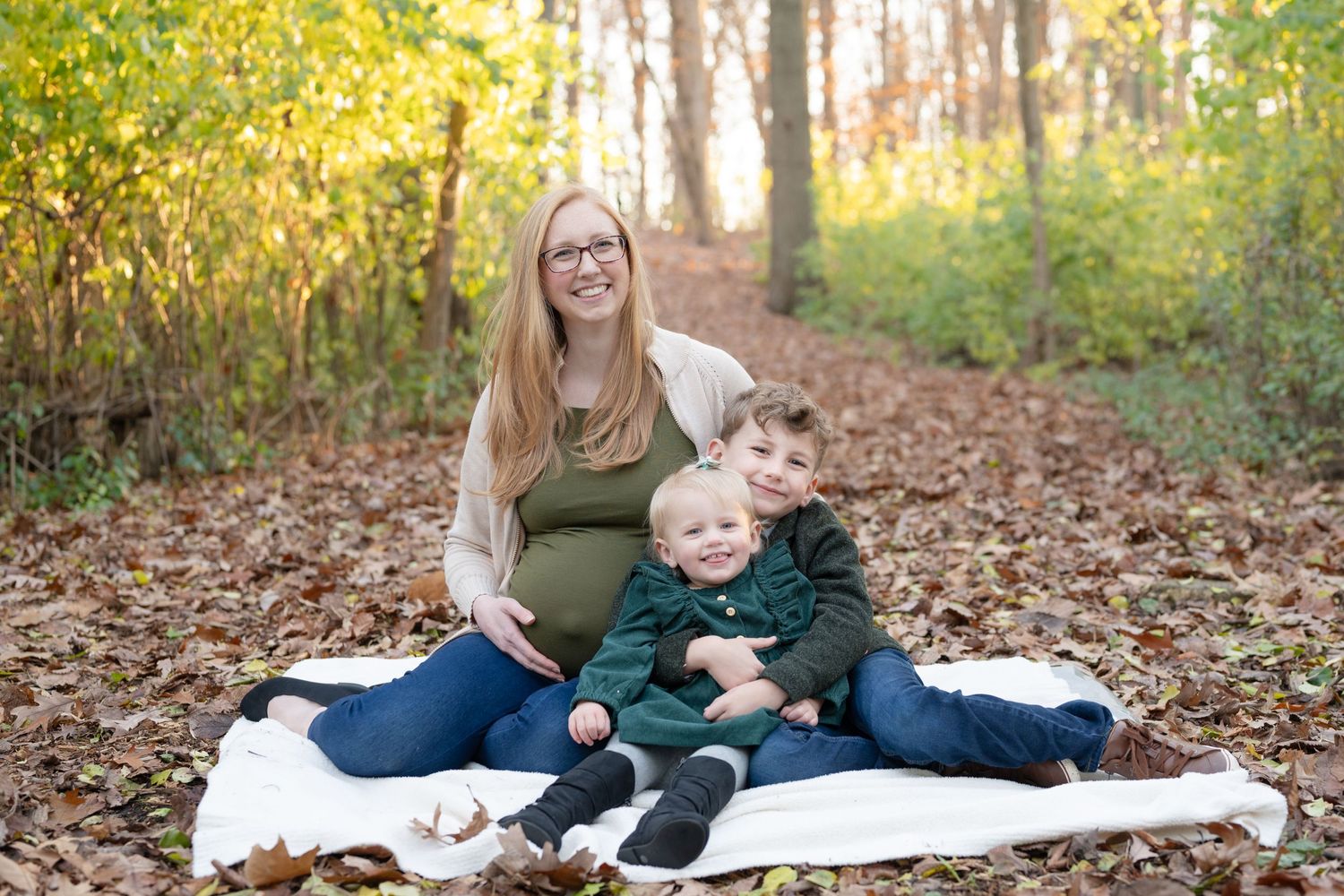 Maternity photo session in a wooded setting with fall foliage and a white blanket on the ground.