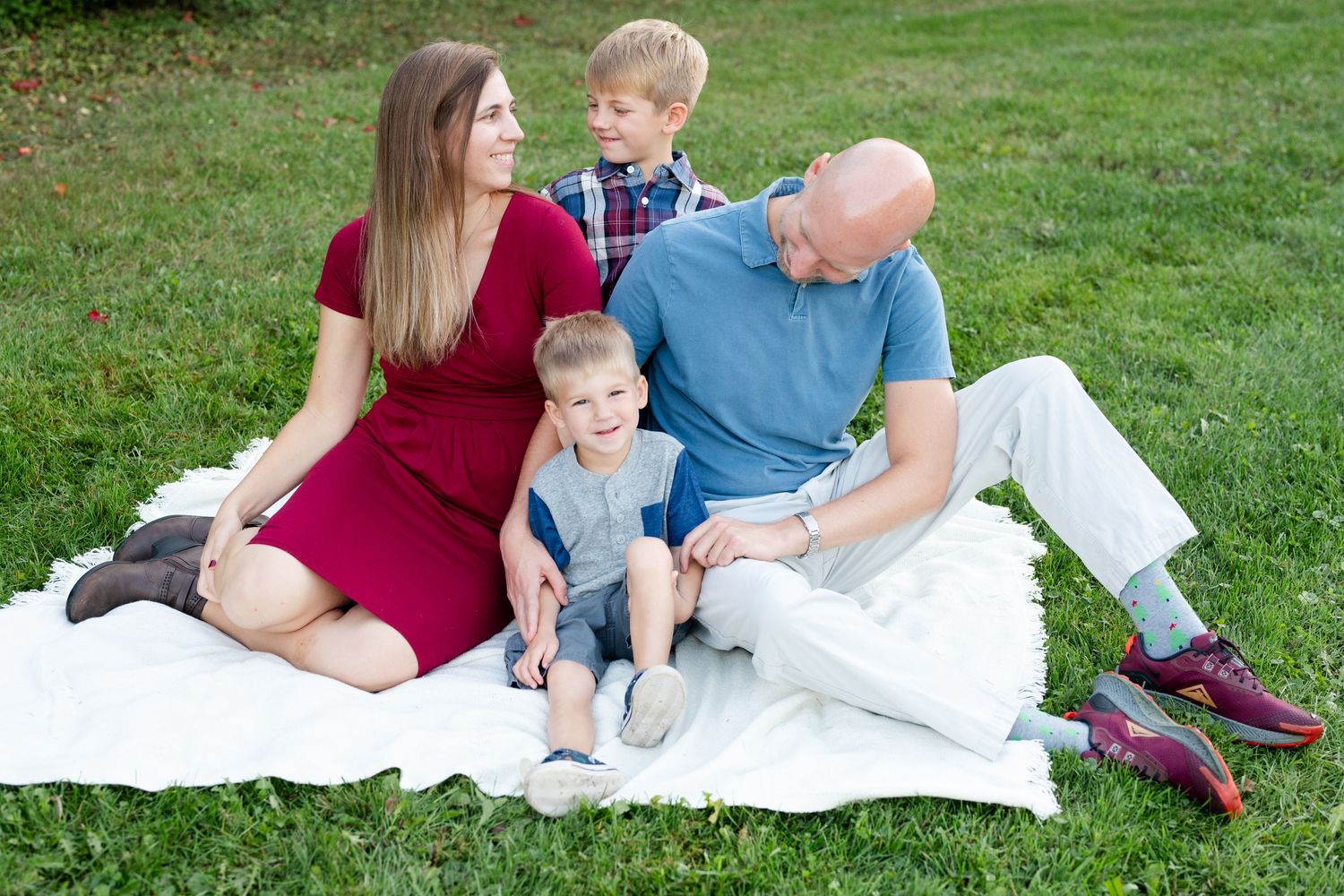 Family gathered together on a white picnic blanket in a sunny park.