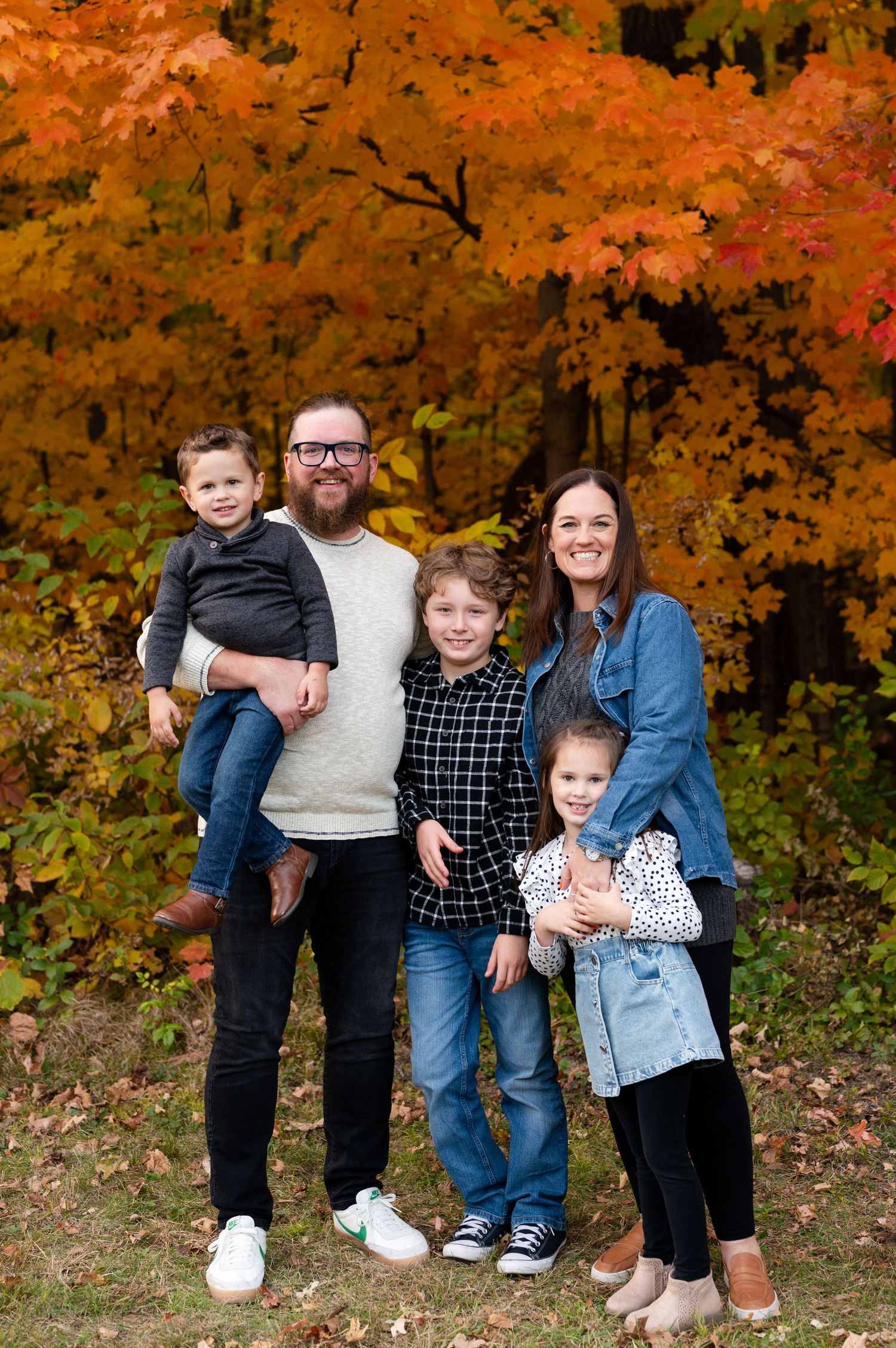 Family group stands together for casual portrait with vibrant fall foliage behind them.