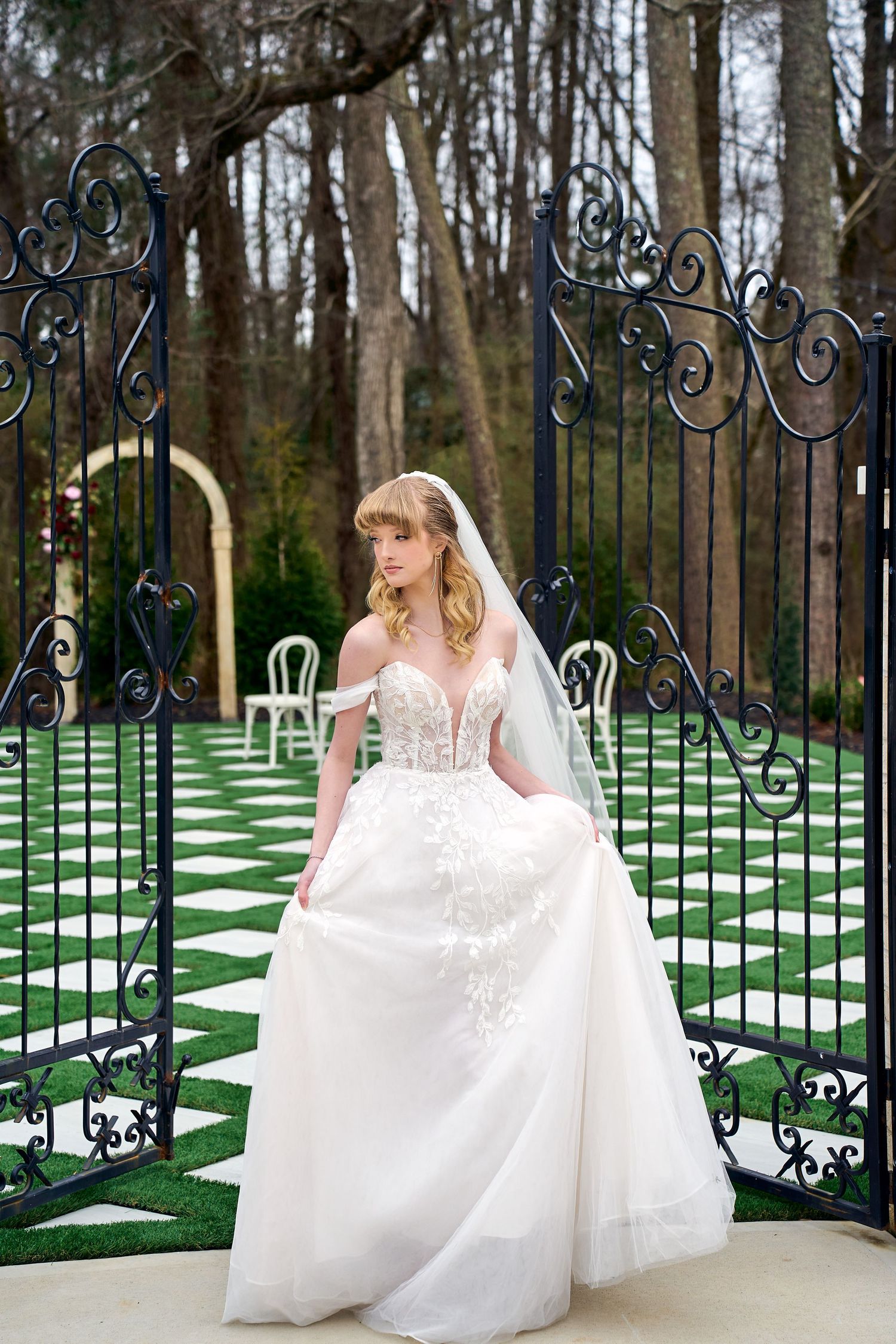 Wedding dress photography showcasing a full white tulle gown with lace bodice against an ornate iron gate and checkerboard lawn.