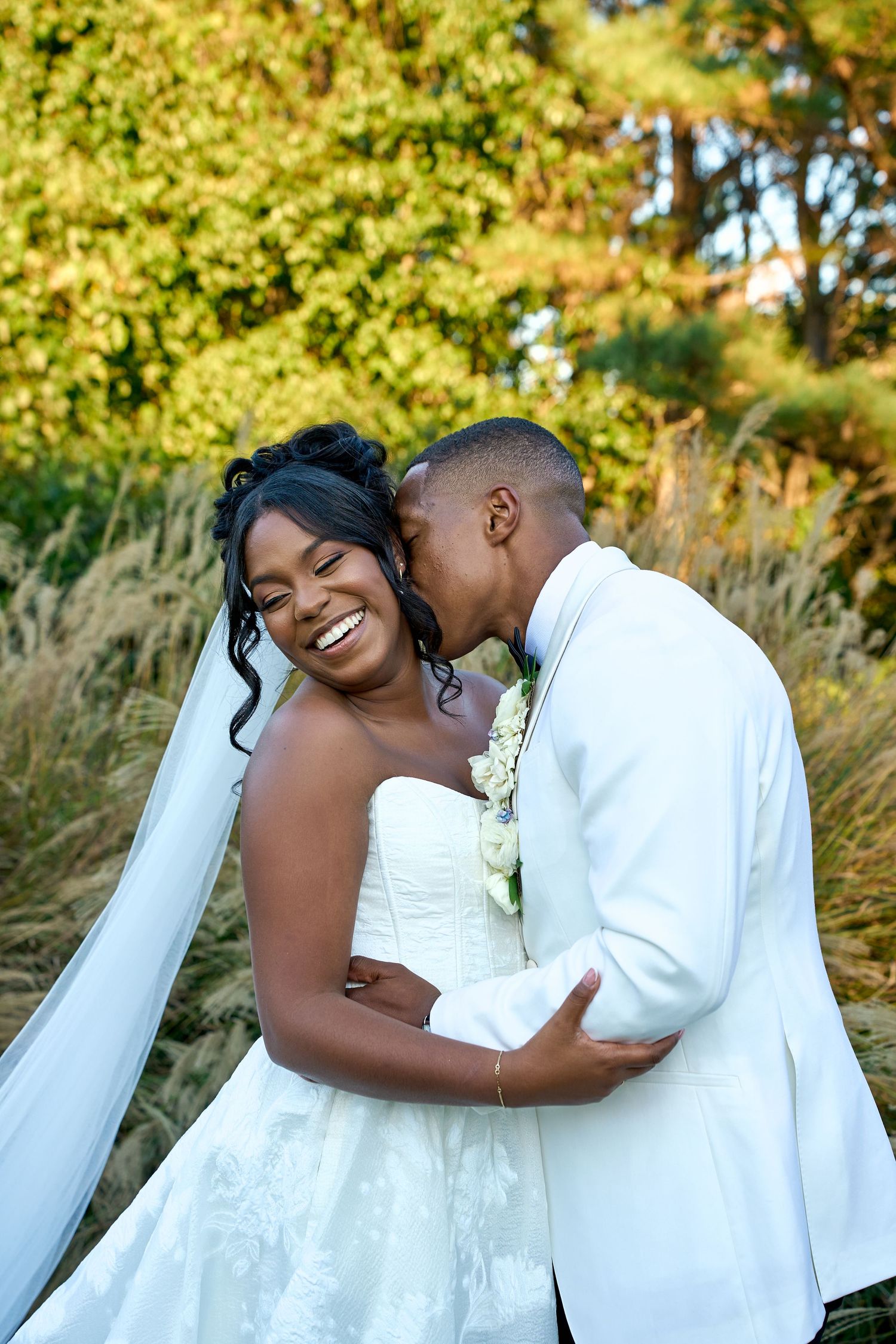 A couple in white wedding attire share joyful moments together in a golden autumn setting.