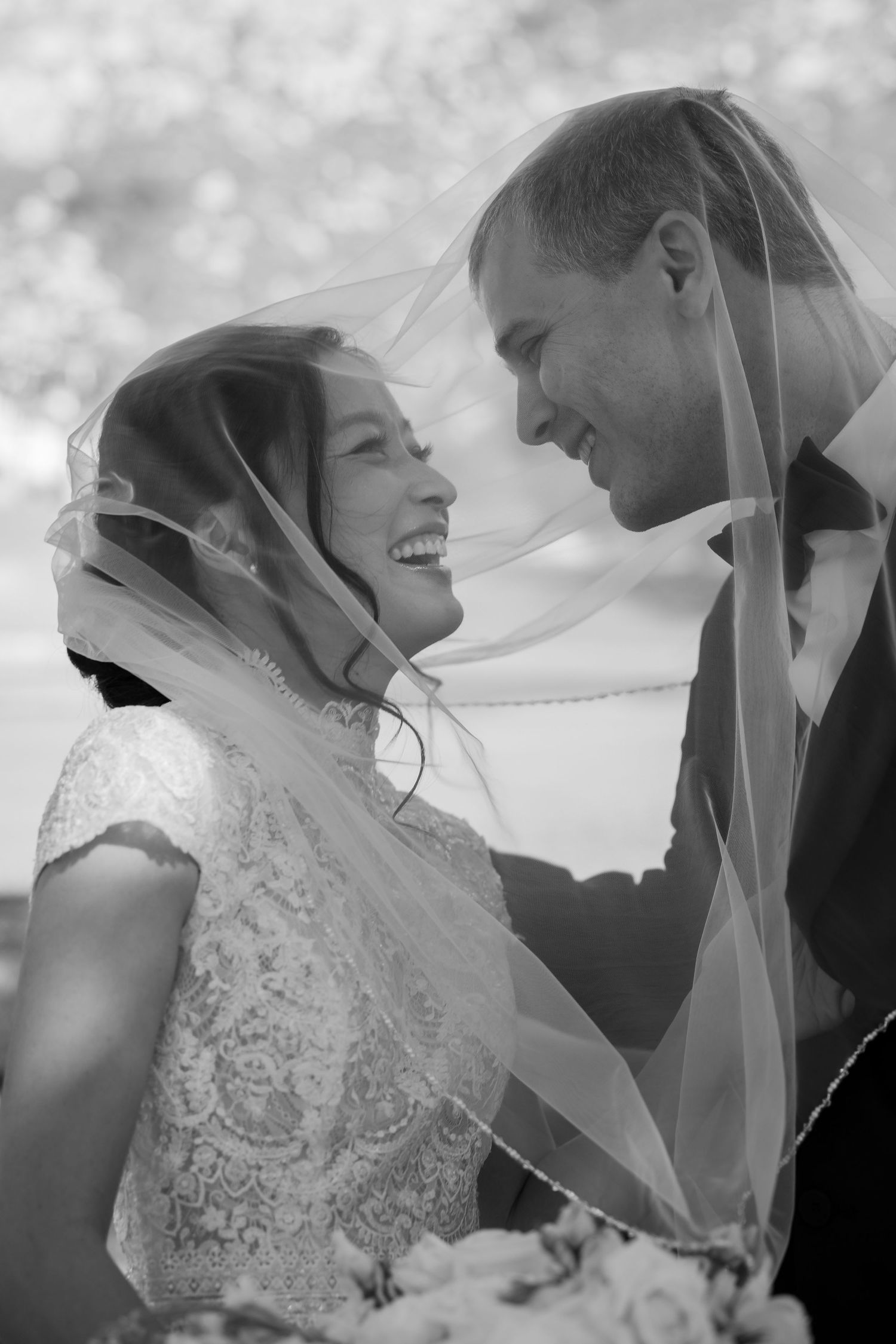 Black and white portrait of smiling bride and groom sharing a joyful moment under the wedding veil.