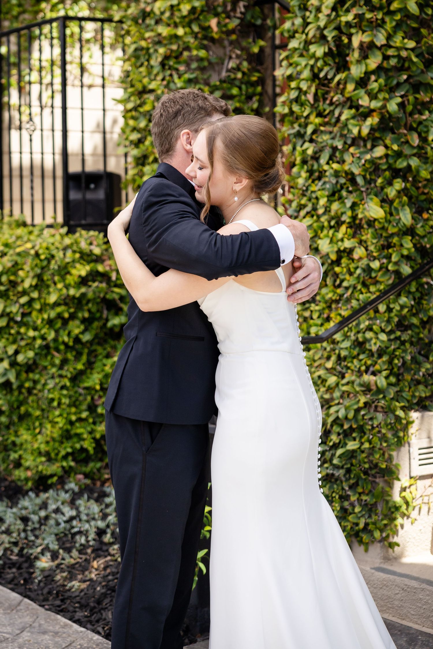 Bride and groom sharing a romantic embrace in front of an ivy-covered wall on their wedding day.