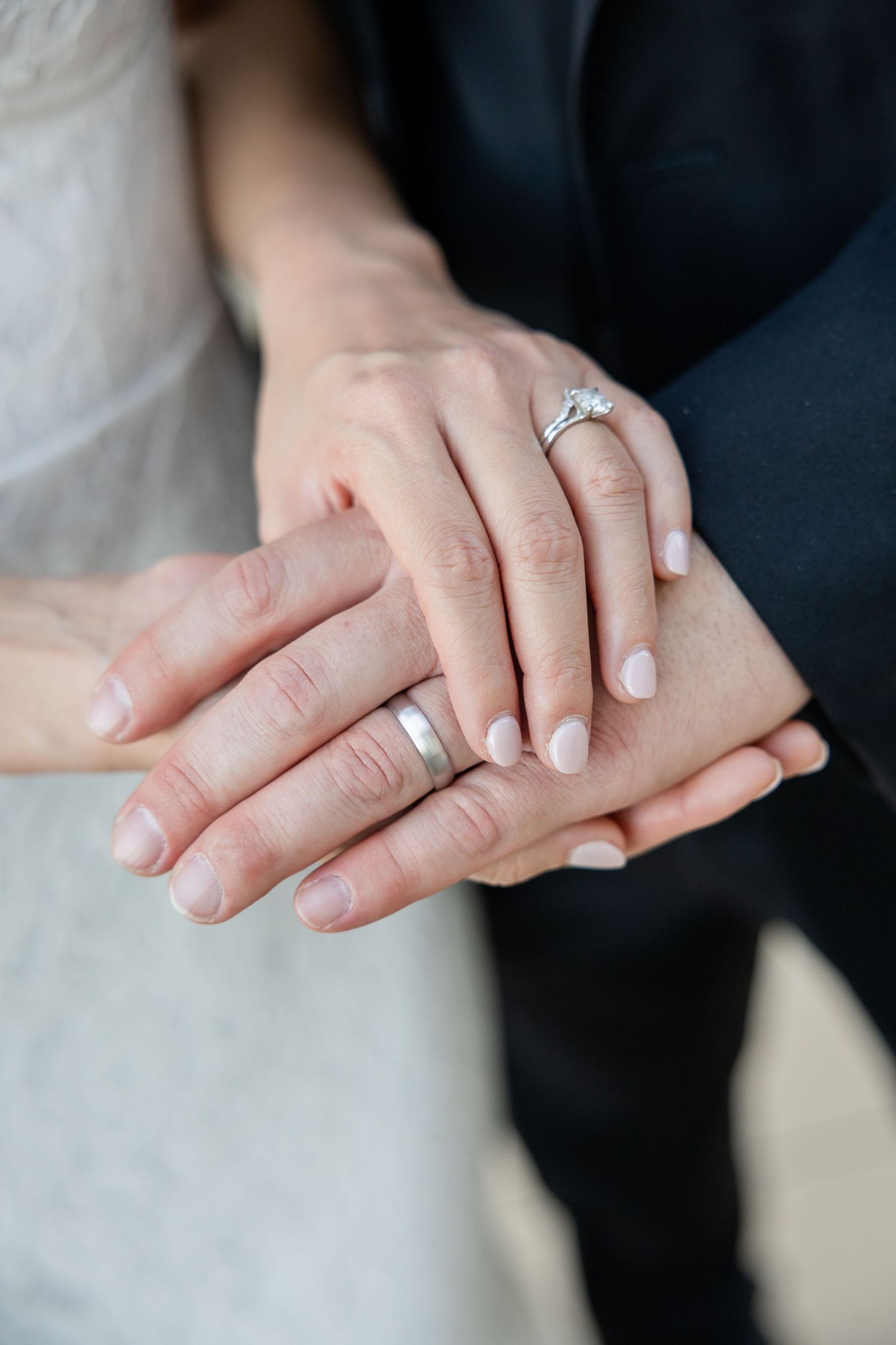 Close-up of newlyweds' hands displaying a diamond engagement ring and matching silver wedding bands.