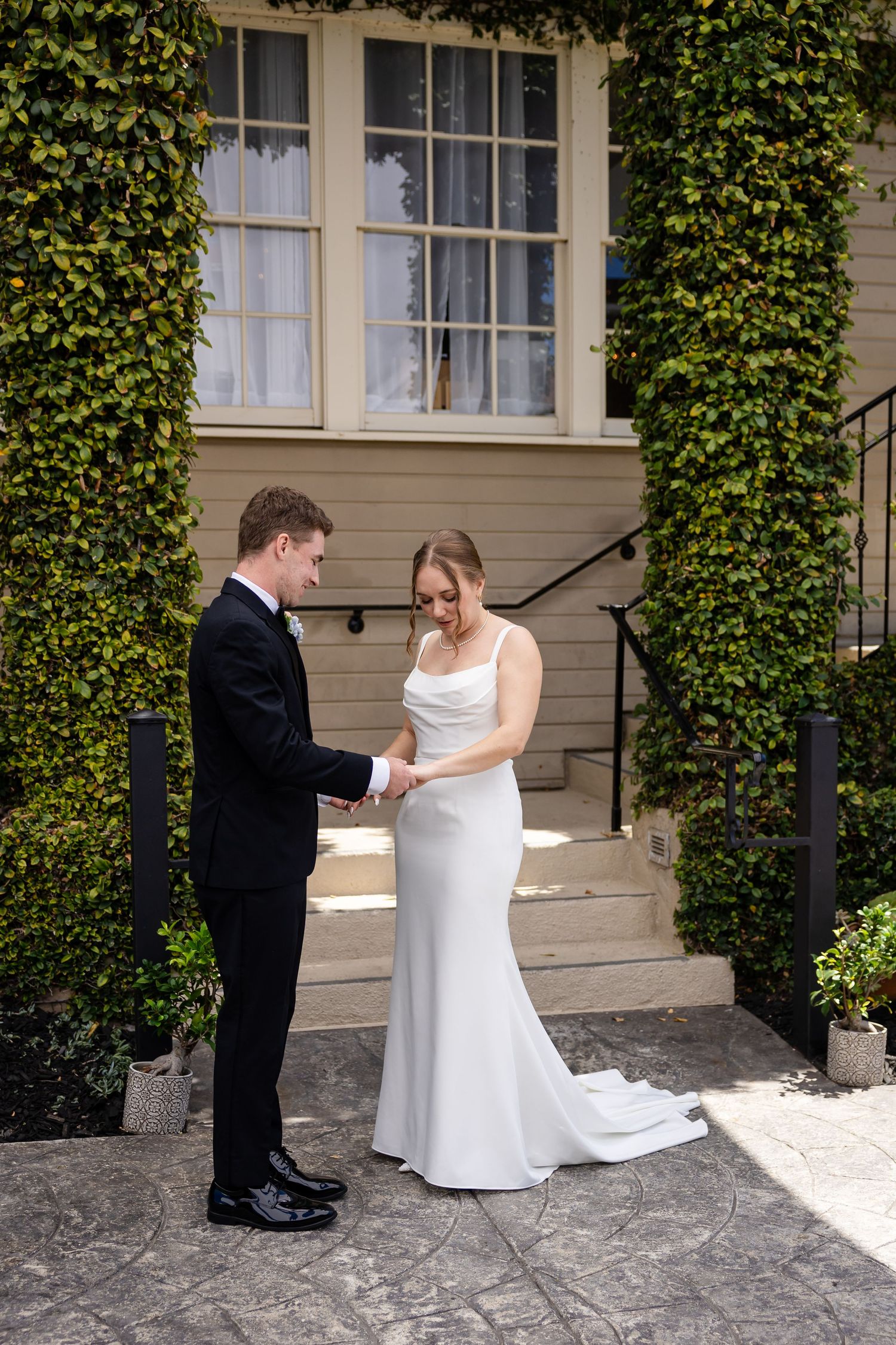 Bride and groom hold hands and look down during intimate first look moment at outdoor wedding venue.