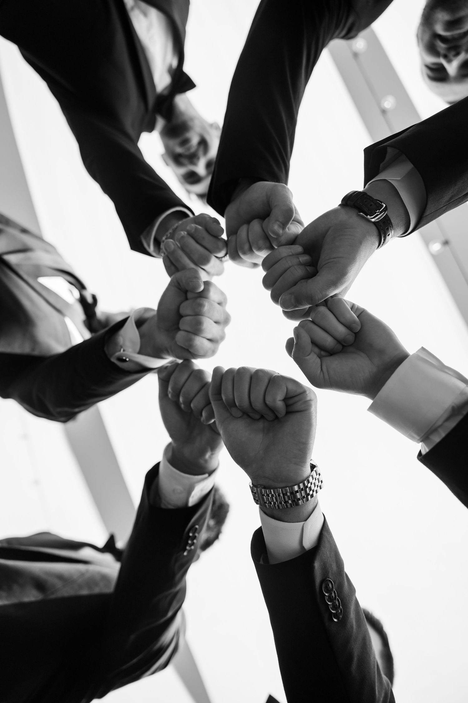 Black and white photo of groomsmen joining fists together in a circle in a show of unity.