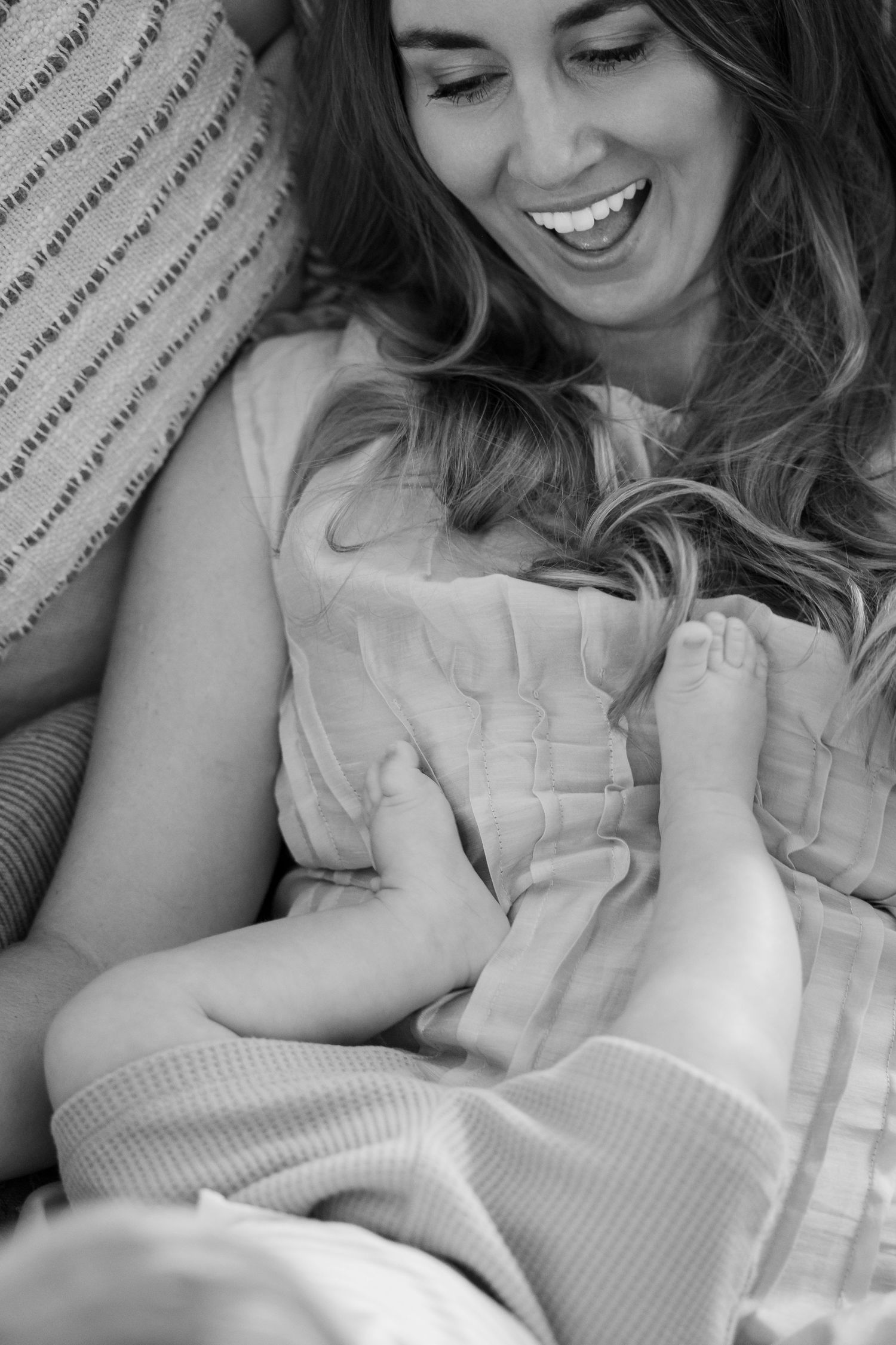 Black and white photo of a laughing mother cradling her young child in her arms while sitting on a couch.