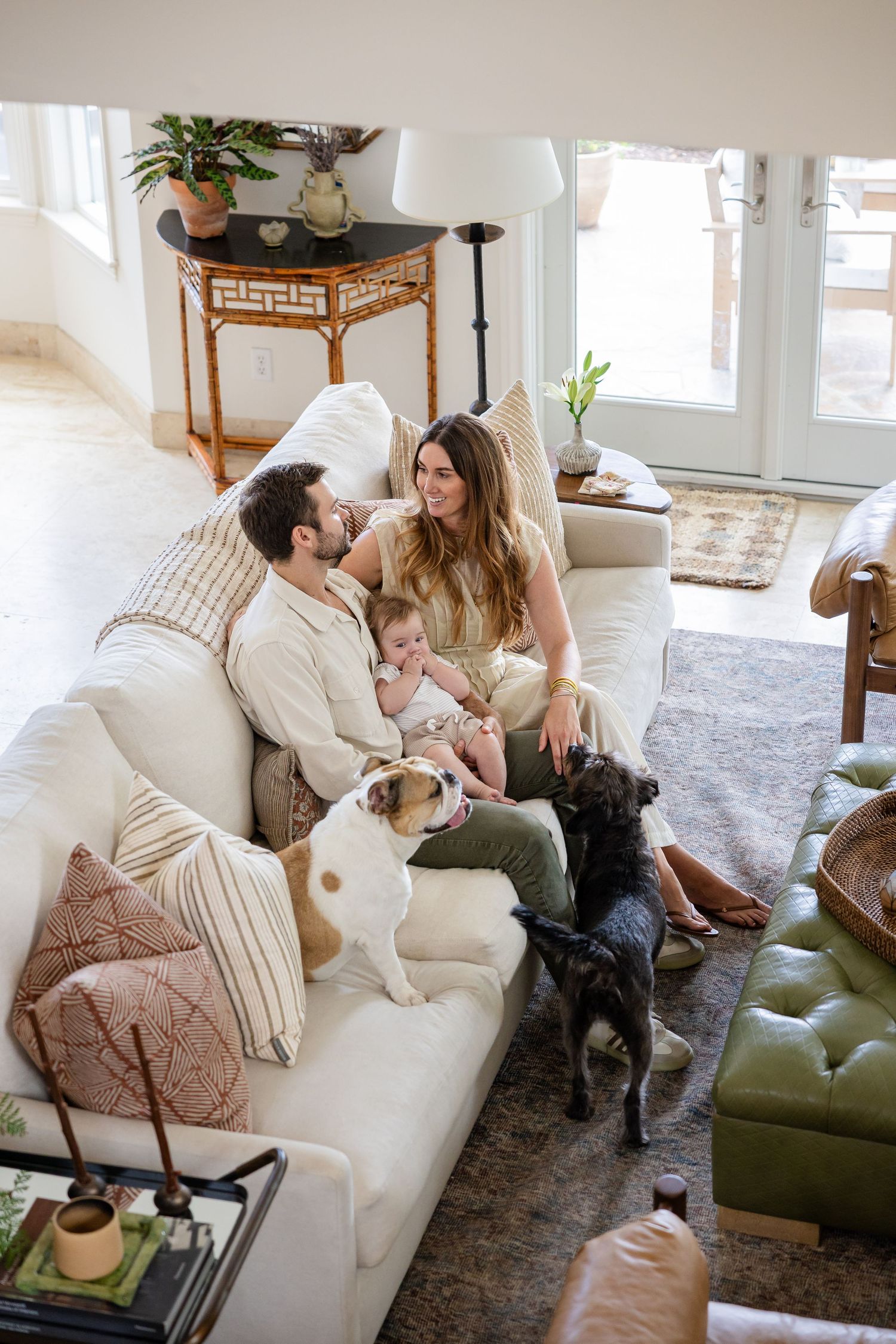 Family with baby and two dogs relaxing together on a white sofa in a bright, cozy living room.