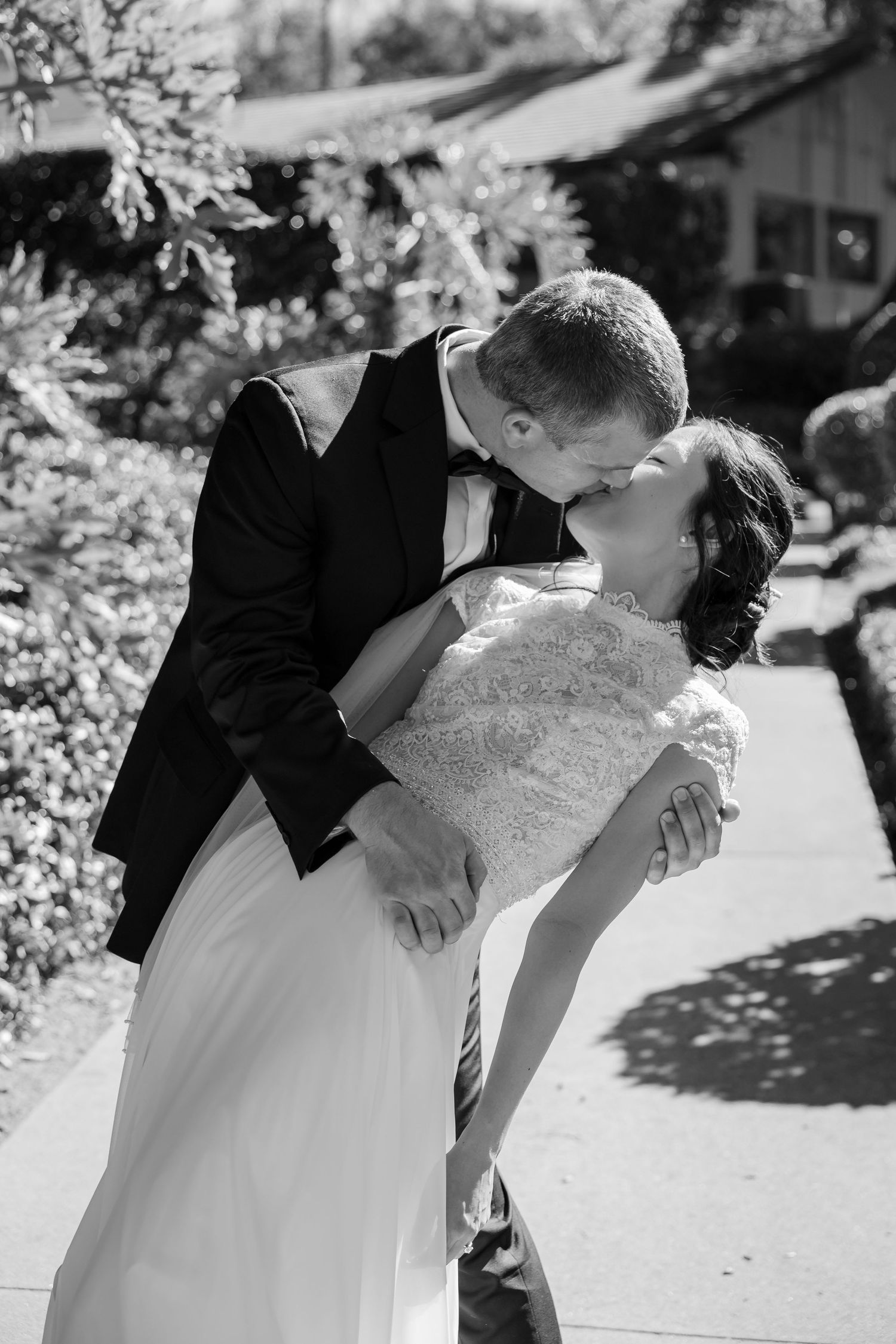 Black and white photo of bride and groom sharing a romantic dip kiss on an outdoor garden pathway.