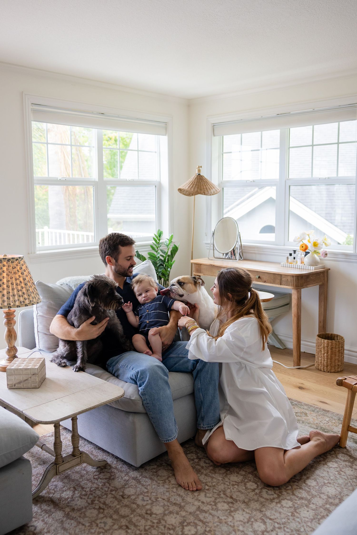 Happy family with baby and two dogs relaxing together on a cozy living room sofa in a bright, modern home.