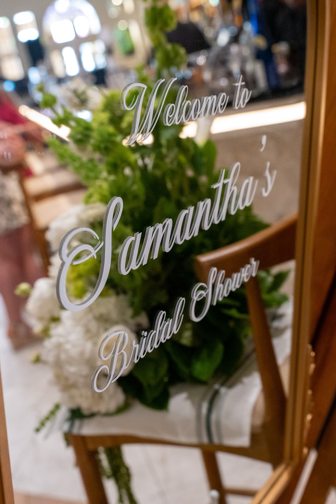 Welcome mirror sign for Samantha's Bridal Shower with white script lettering and lush green and white floral decor.