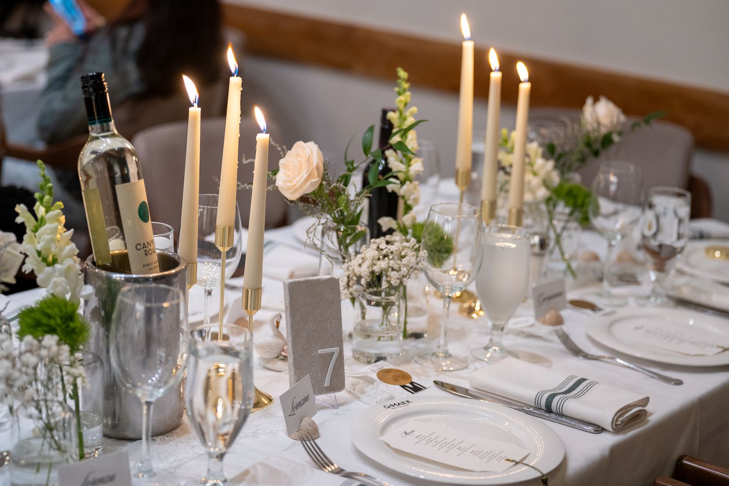 Elegant wedding reception table with lit taper candles, white floral centerpieces, champagne flutes, and table number 7.