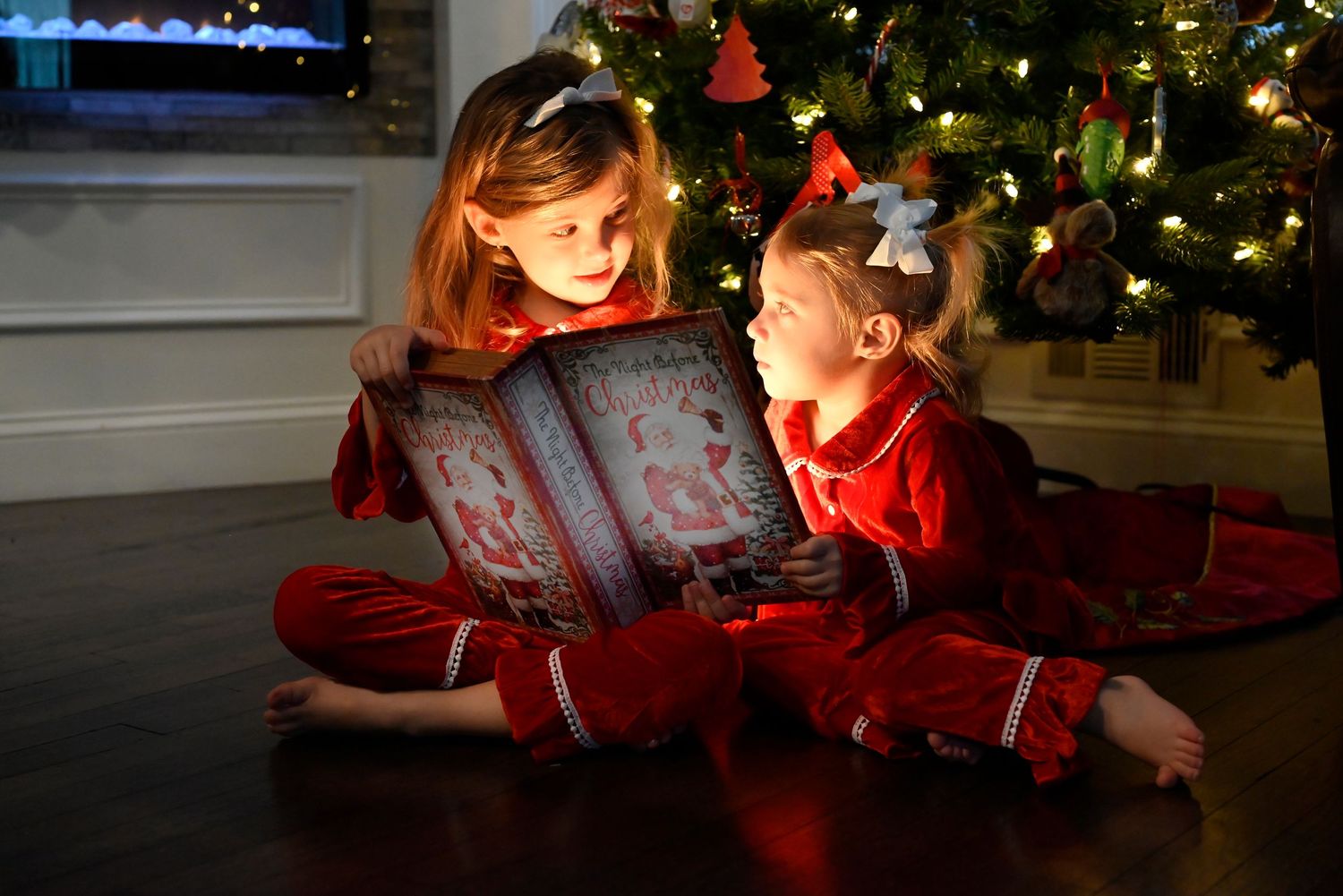 Child in red pajamas reading book by Christmas tree
